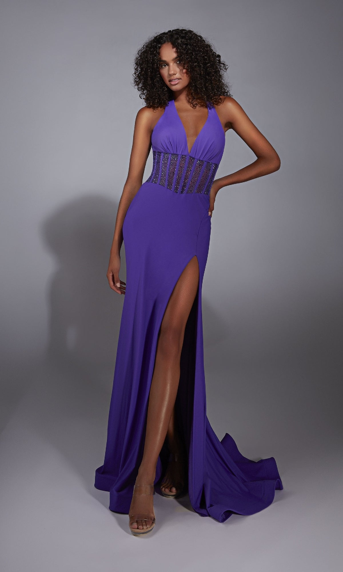 A woman poses against a plain gray background wearing the Alyce 61860 Long Prom Dress, a sleeveless, floor-length purple gown featuring a corset bodice and thigh-high slit.