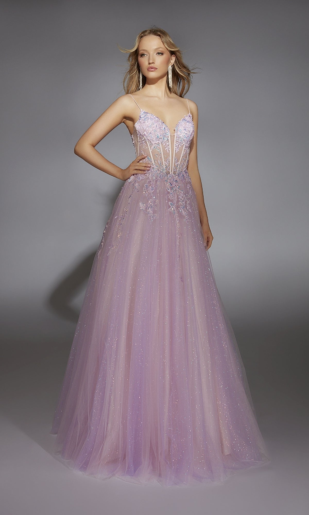 A woman stands against a gray backdrop in the Alyce 61865 long prom dress—a lilac gown featuring sheer panels, floral appliqué, and a delicate corset bodice.