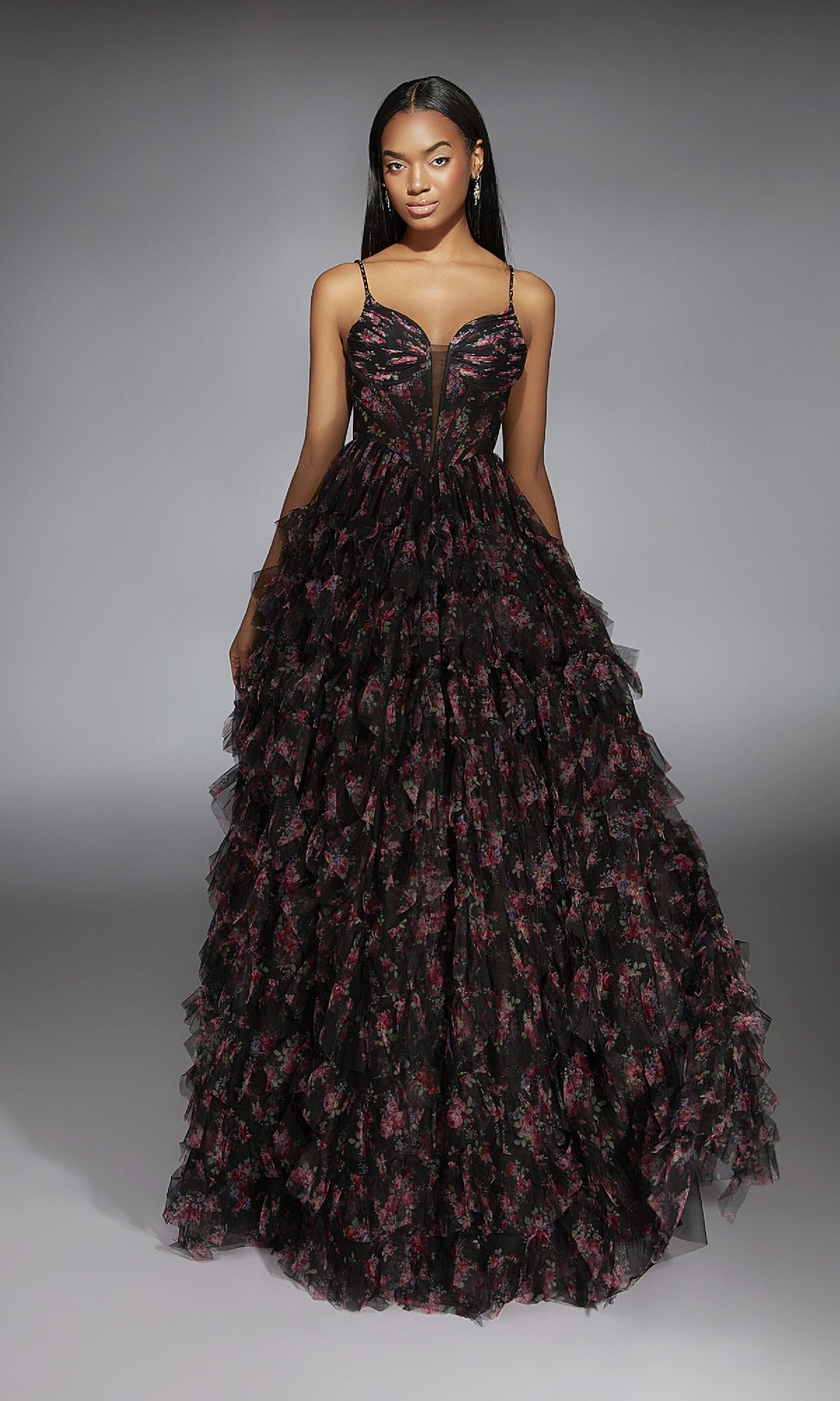 A woman models the Alyce 61866 long prom dress, featuring black fabric with red floral print, spaghetti straps, and a ruffle-tiered A-line skirt, standing against a neutral background.