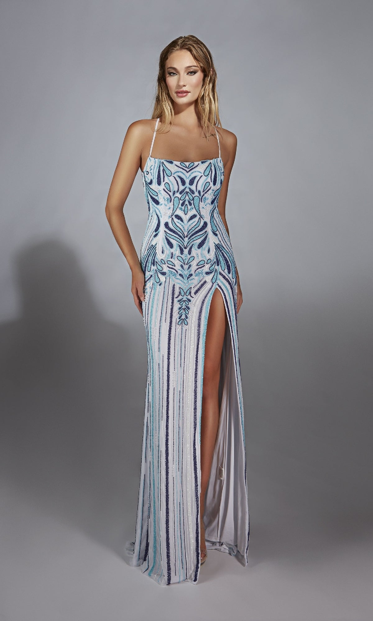 A woman models the Alyce 61868, a floor-length sleeveless prom dress with blue and silver sequins, a square neckline, and high leg slit, standing against a plain gray background.