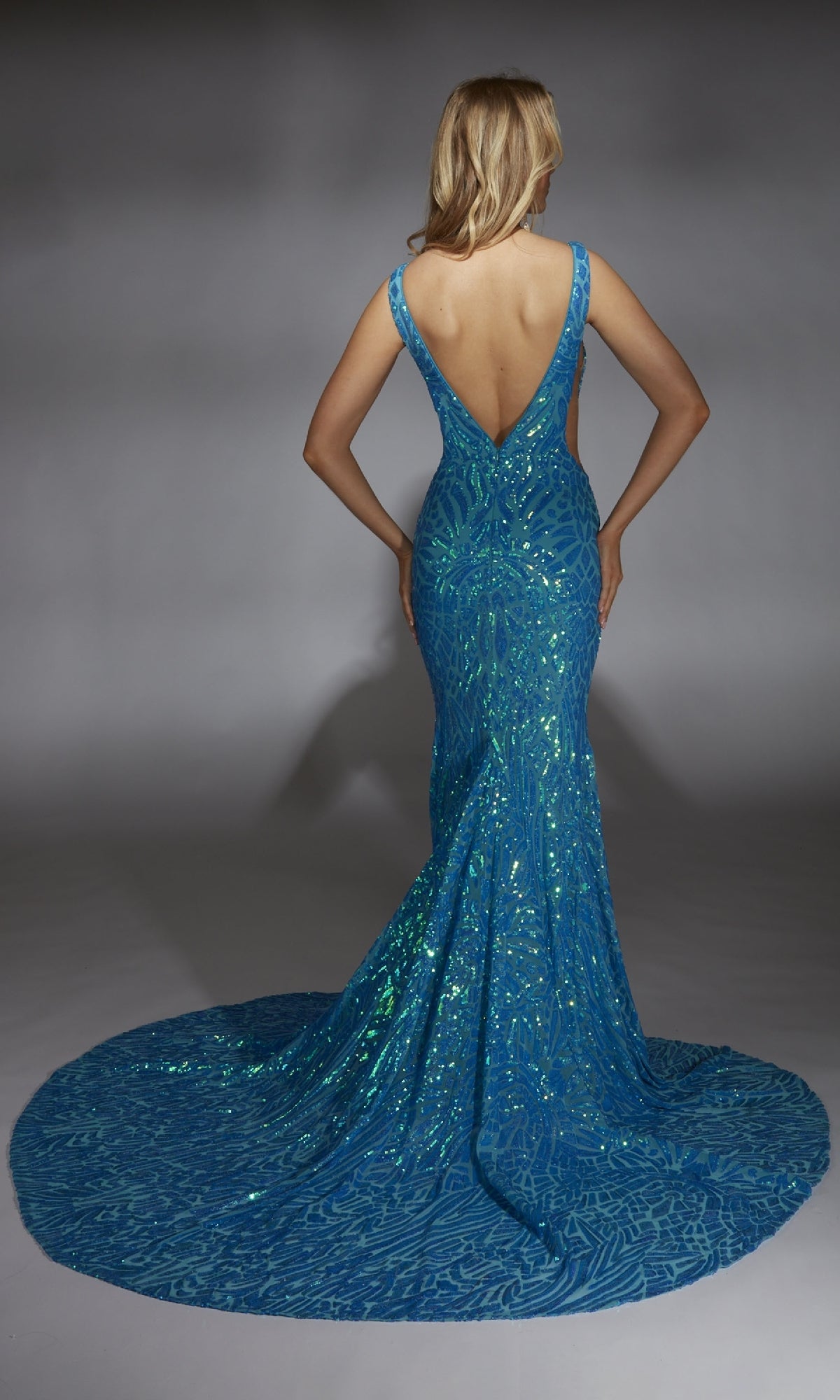 A model with blonde hair wears the Alyce 61876 long prom dress, featuring blue sequins, a deep V-back, and a long train, posed against a neutral background.