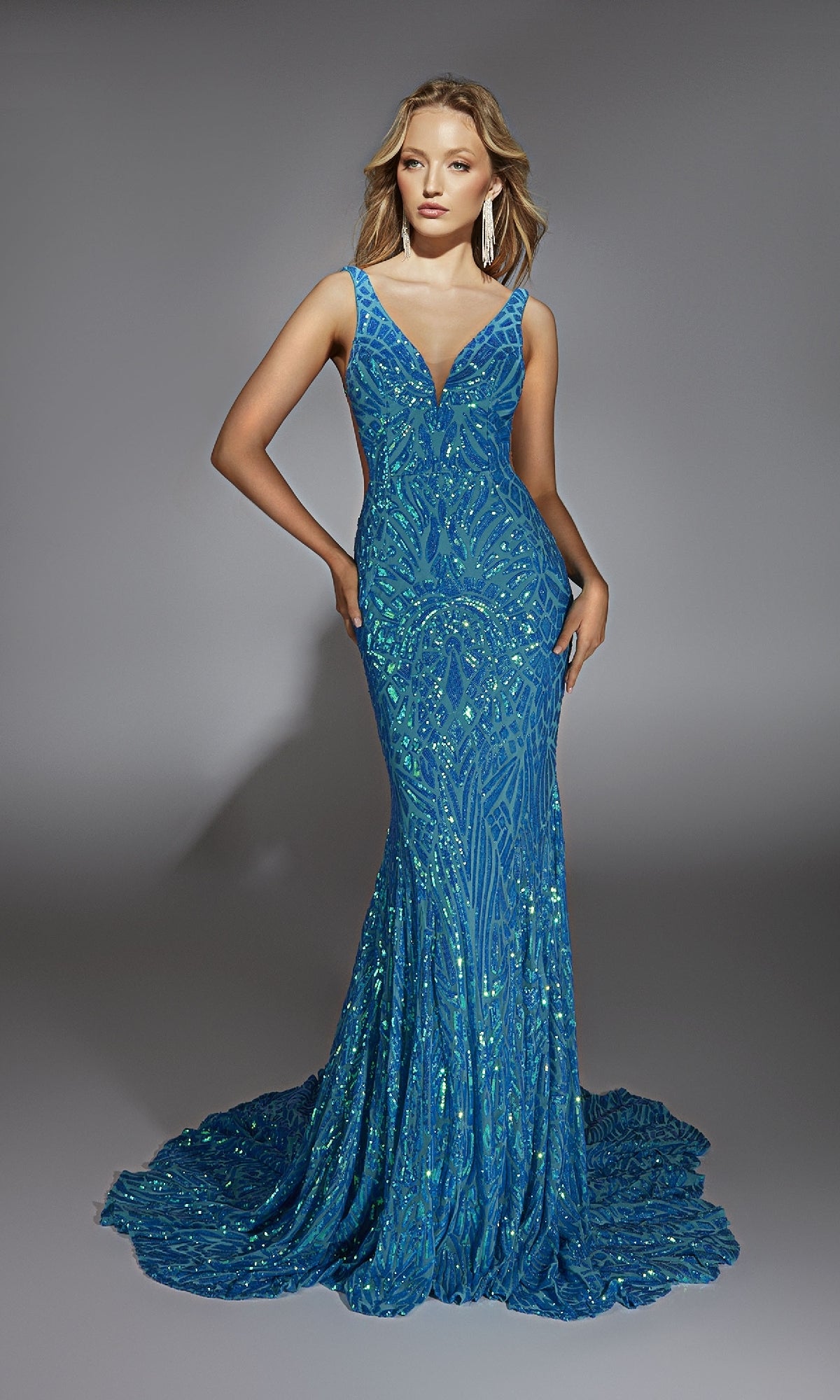 A woman poses in the Alyce 61876 long prom dress, featuring sparkling sequins, a deep V-neckline, open back, fitted silhouette, and slight train against a plain gray background.