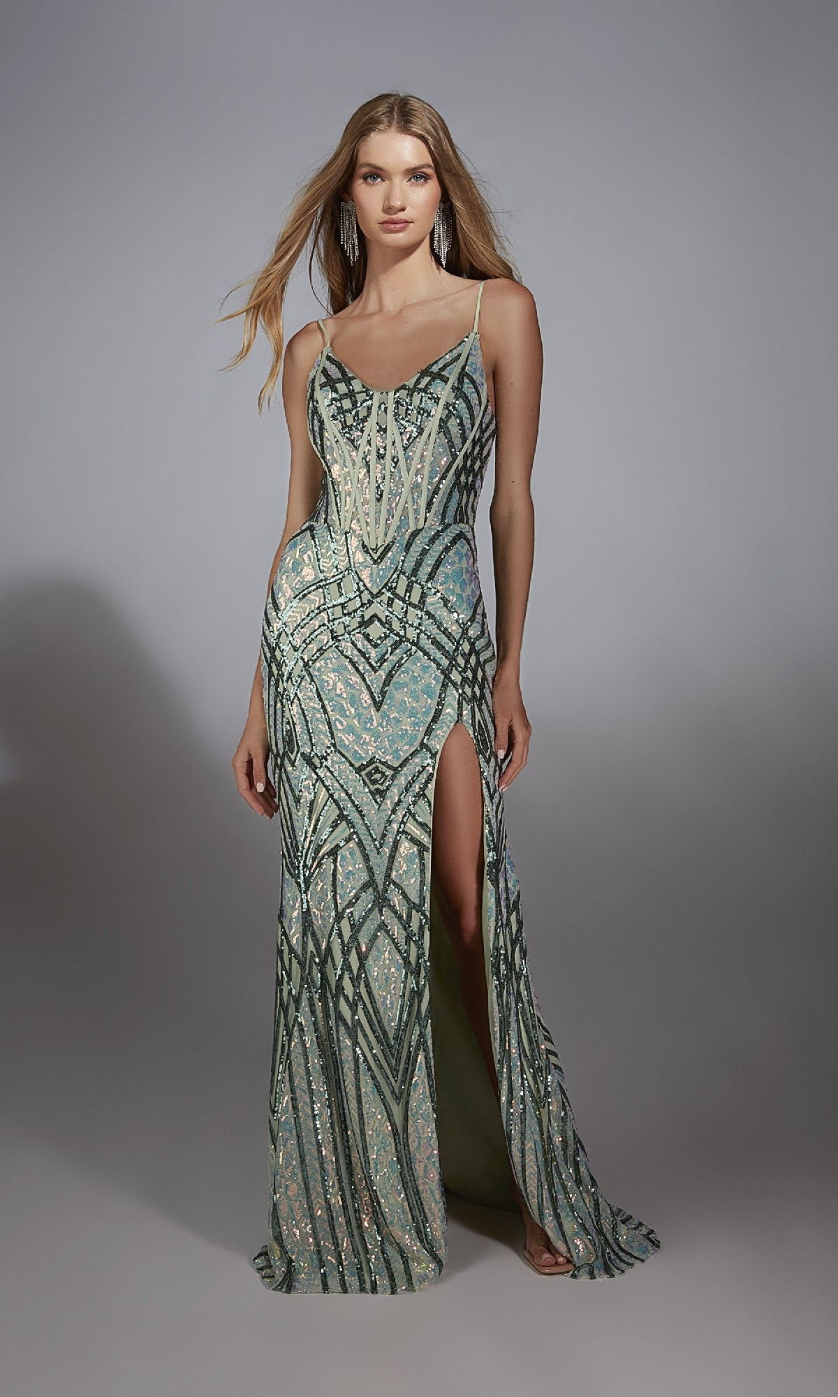 A woman in the Alyce 61920 long prom dress—sleeveless, floor-length, with geometric sequin patterns, a high slit, and lace-up back—stands against a plain gray background.