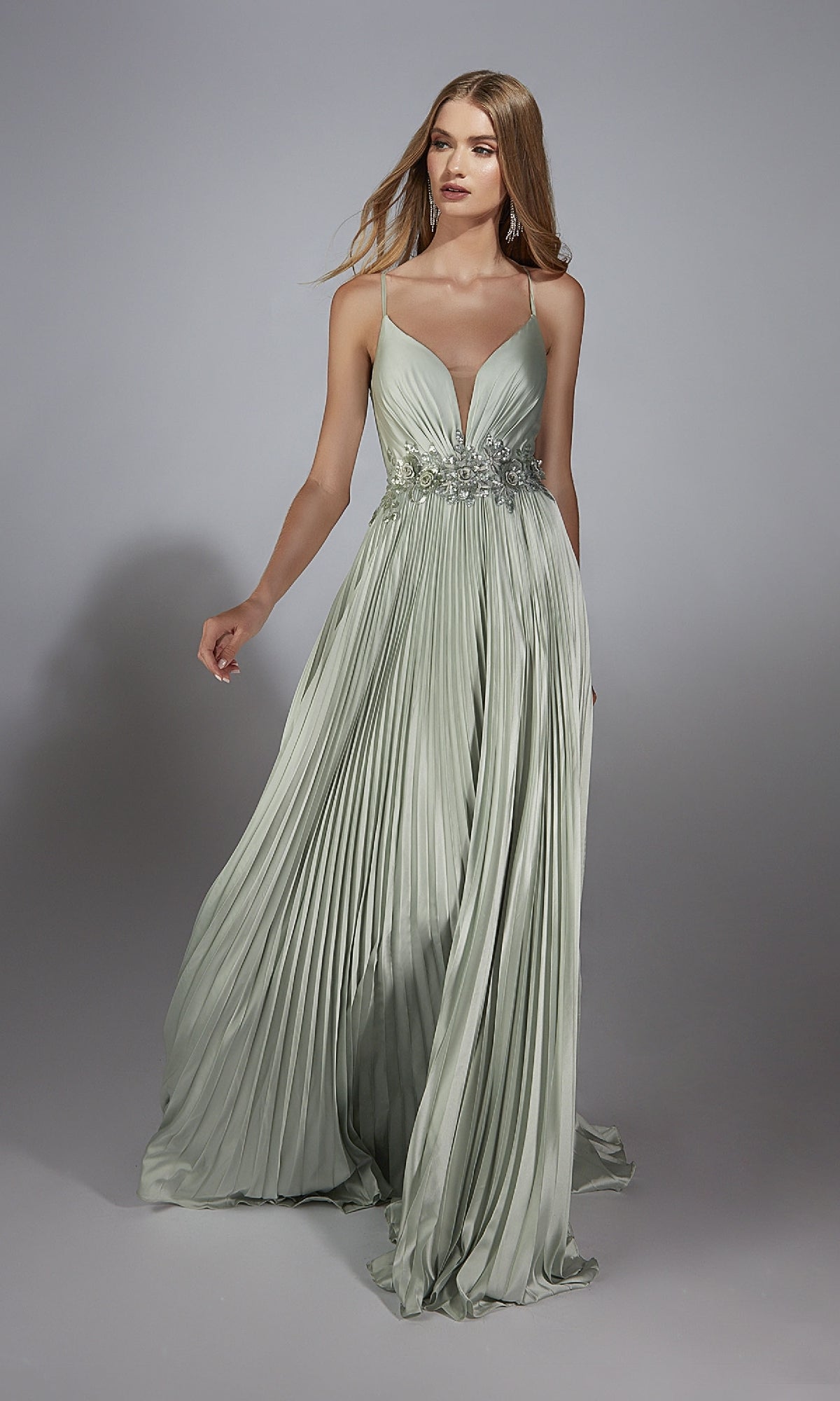 A woman stands against a plain gray background wearing the Alyce 61923 Long Prom Dress—a light green, floor-length A-line gown with thin straps, pleats, and a deep V-neckline.