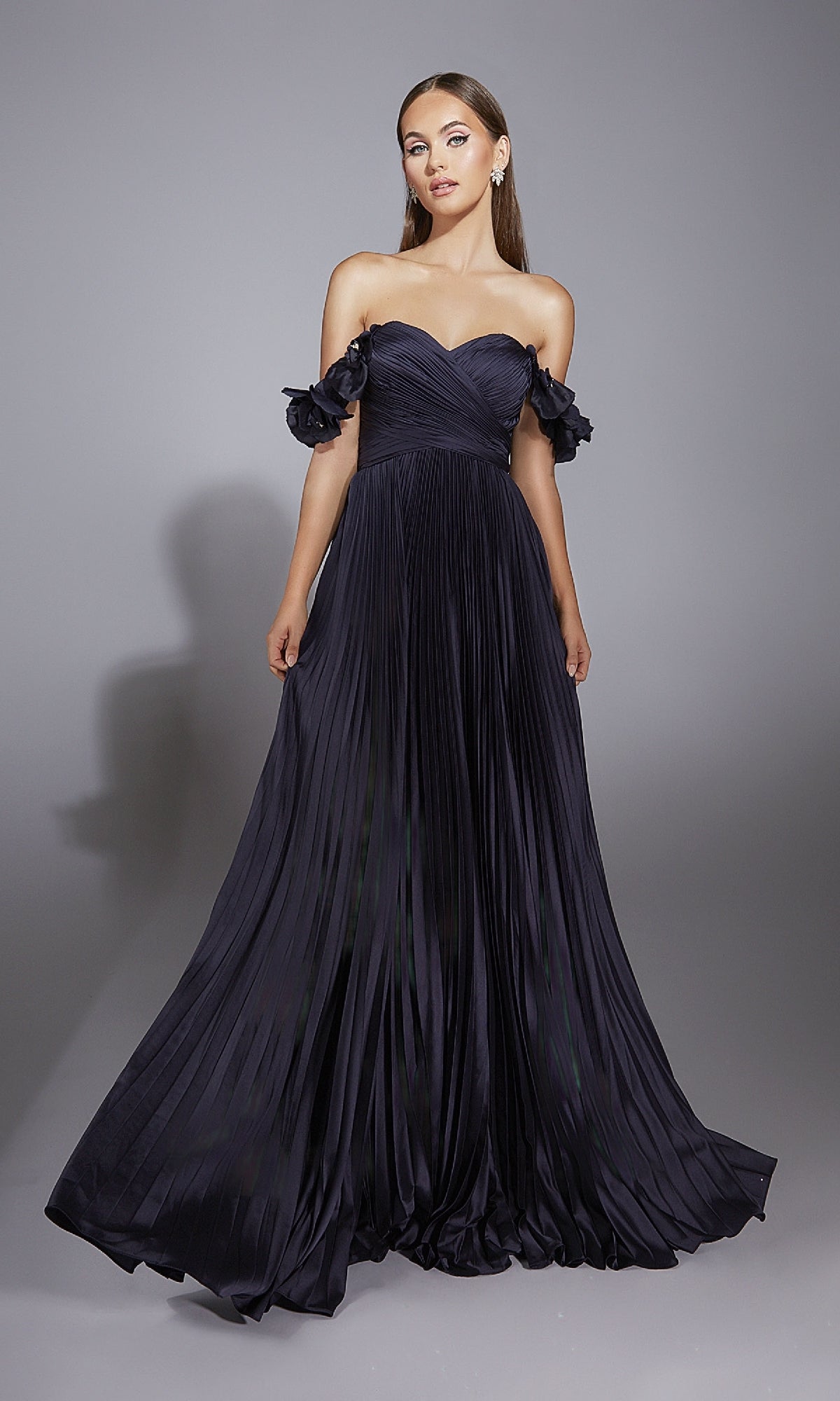 A woman models the Alyce 61946 long prom dress—an off-the-shoulder, floor-length pleated A-line gown—against a plain gray background.