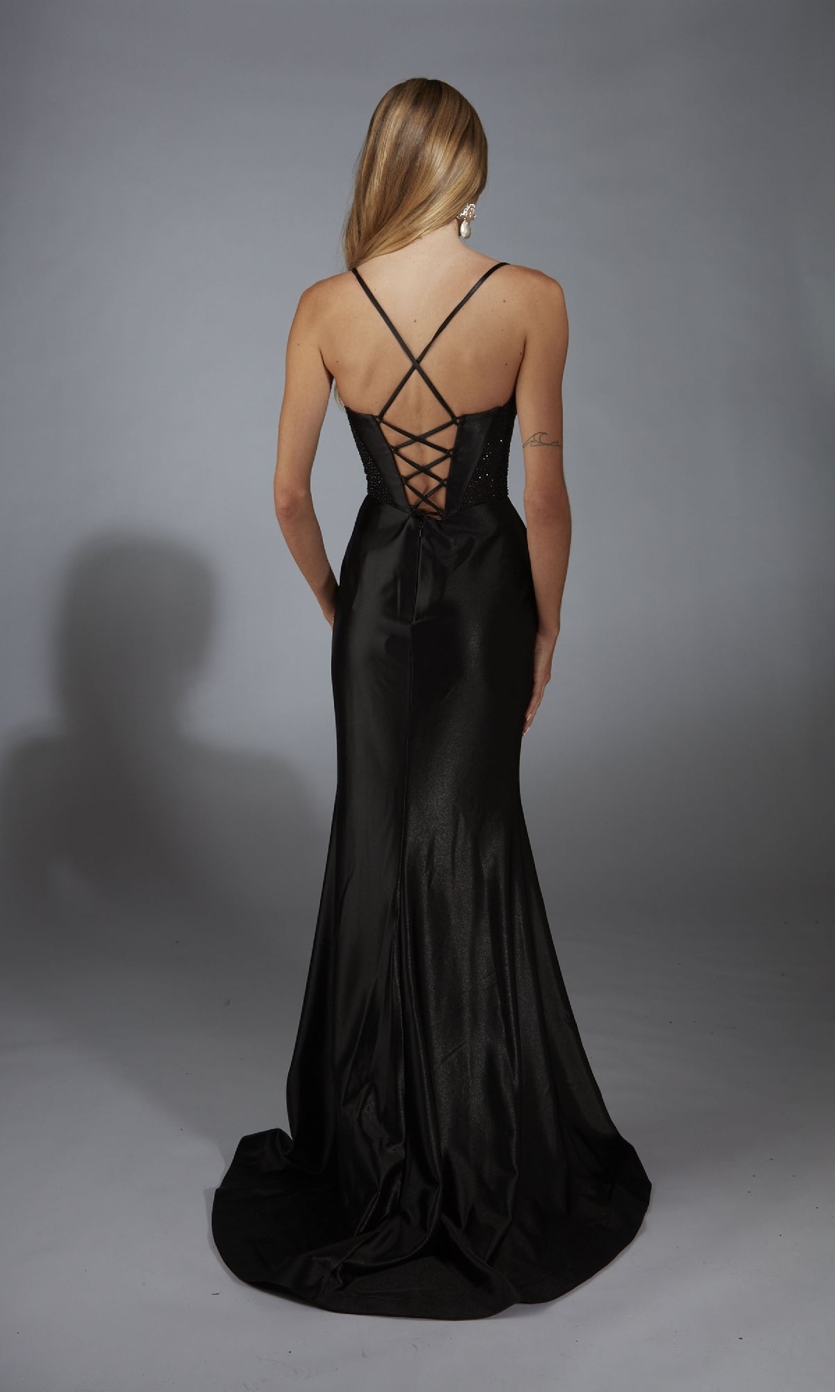 A person faces away from the camera in a long formal dress with spaghetti straps and a lace-up back, highlighting the elegant silhouette of the Alyce 61950 Lace-Up Long Corset Prom Dress against a neutral background.