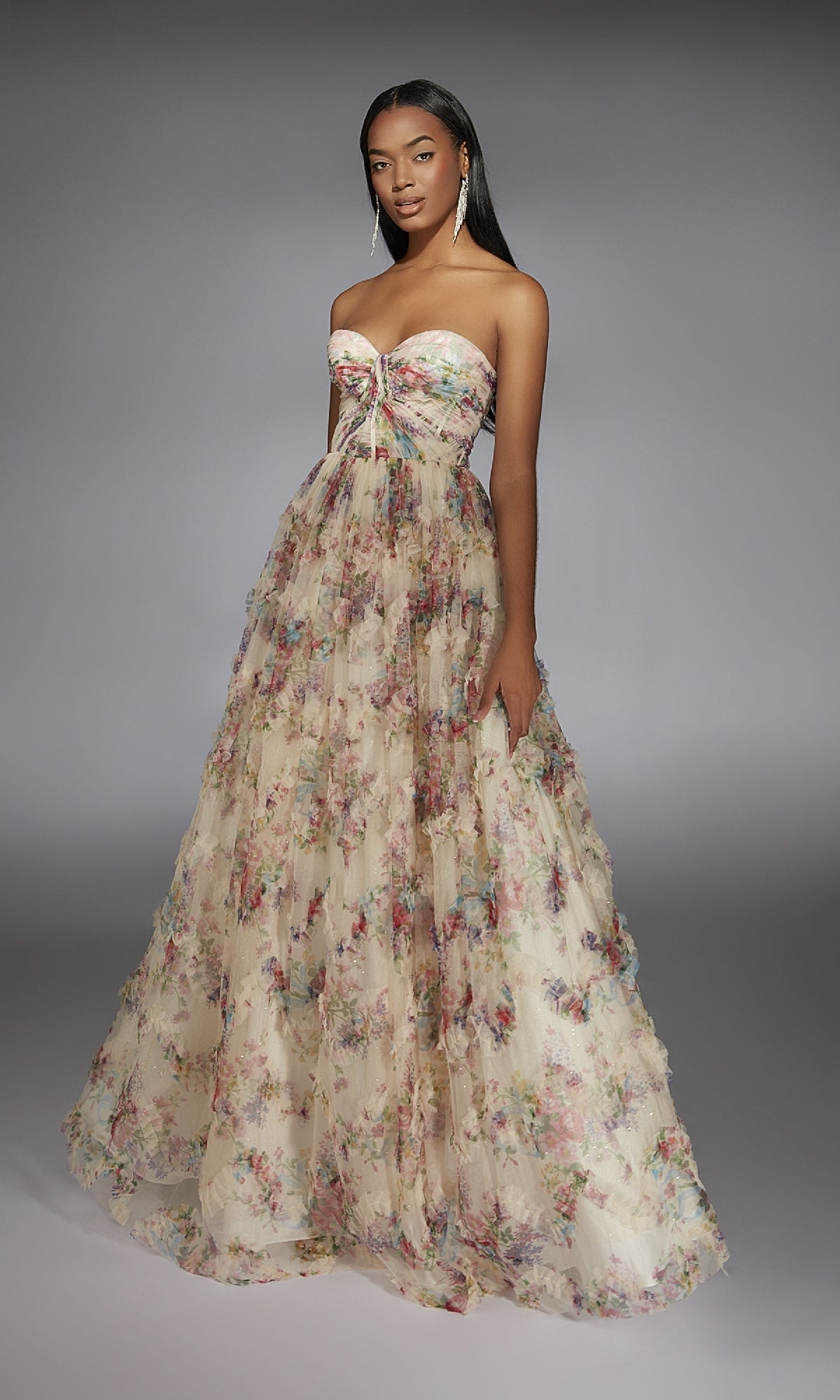 A woman wears the Alyce 61957 long prom dress, featuring a strapless corset bodice and sheer ruffled layers over an A-line skirt, set against a plain gray background.