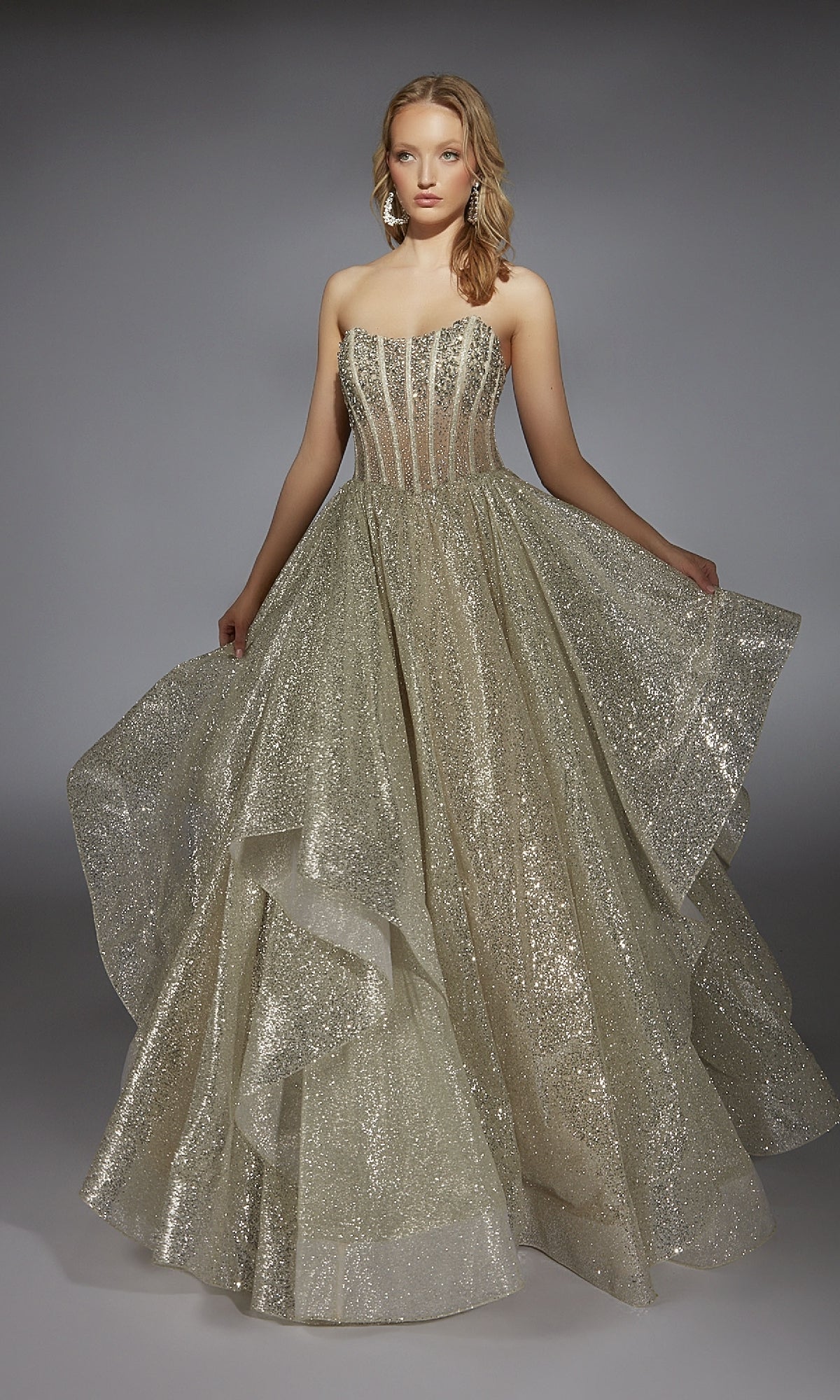 A woman wears the Alyce 61971 long prom dress, showcasing a strapless beaded corset bodice and a floor-length gold glitter skirt with voluminous layers.