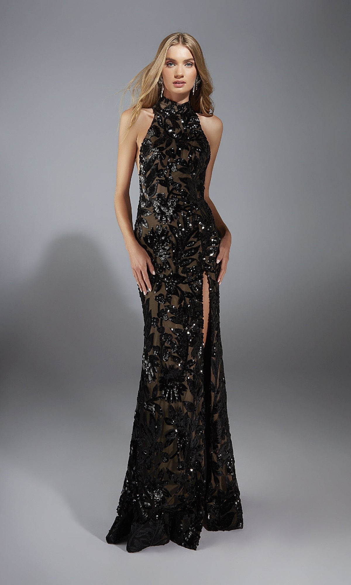 A woman models the Alyce 61979 long prom dress, a sleeveless black sequin gown with a high neck and thigh-high slit, standing against a plain gray background.