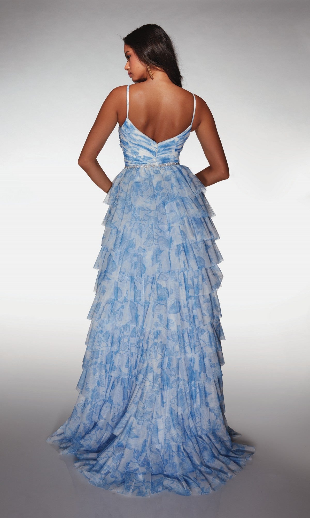 A woman stands facing away, wearing the Alyce 62018 Long Prom Dress in light blue and white, featuring spaghetti straps, a v-shaped back, and elegant tiered ruffles reminiscent of an A-line silhouette.