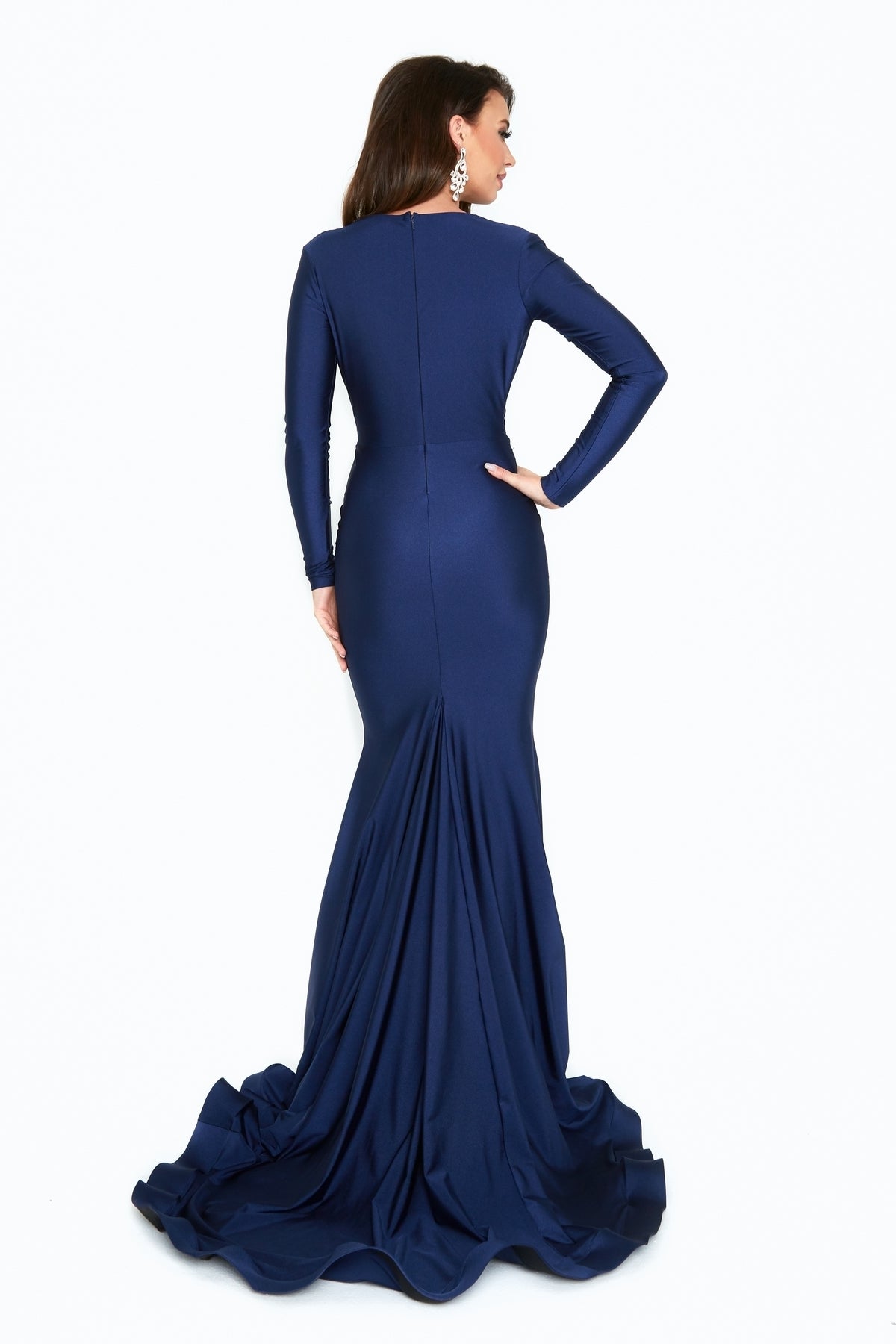 A woman in an Atria 6201H Long Sleeve Long Formal Dress stands facing away from the camera, showcasing its fitted bodice and flared train against a white background.