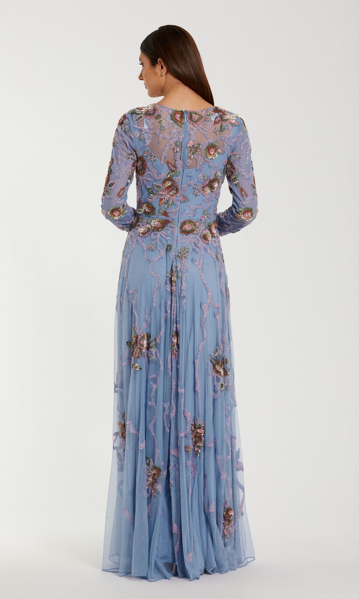 A woman facing away, wearing the Mac Duggal 6202 long formal dress in light blue, featuring sheer sleeves and intricate floral embroidery, stands against a plain light background.