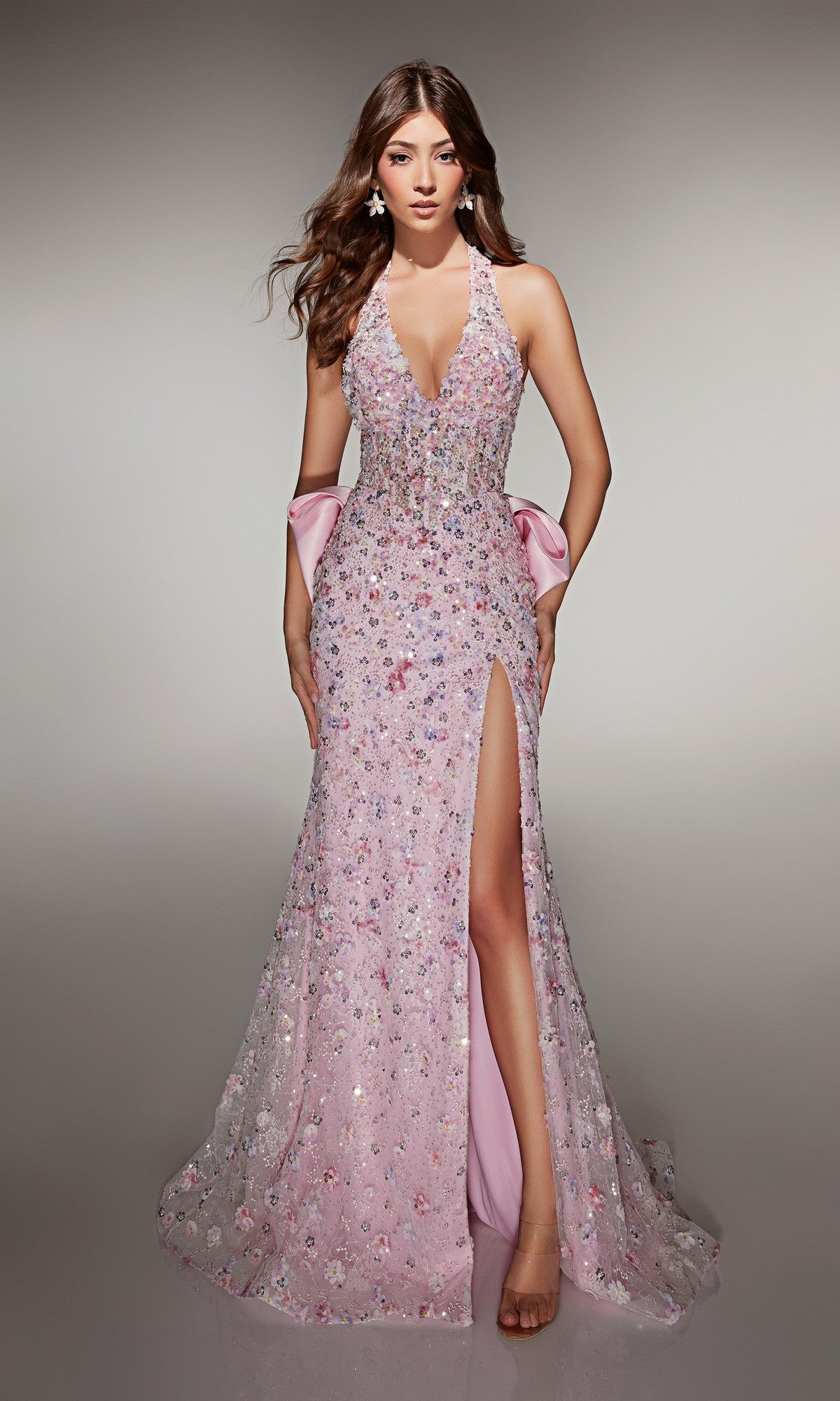 A woman stands against a neutral background in the Alyce 62044 long pink prom dress, featuring sequin embellishments, sleeveless design, deep V-neckline, high slit, and a satin bow at the back.