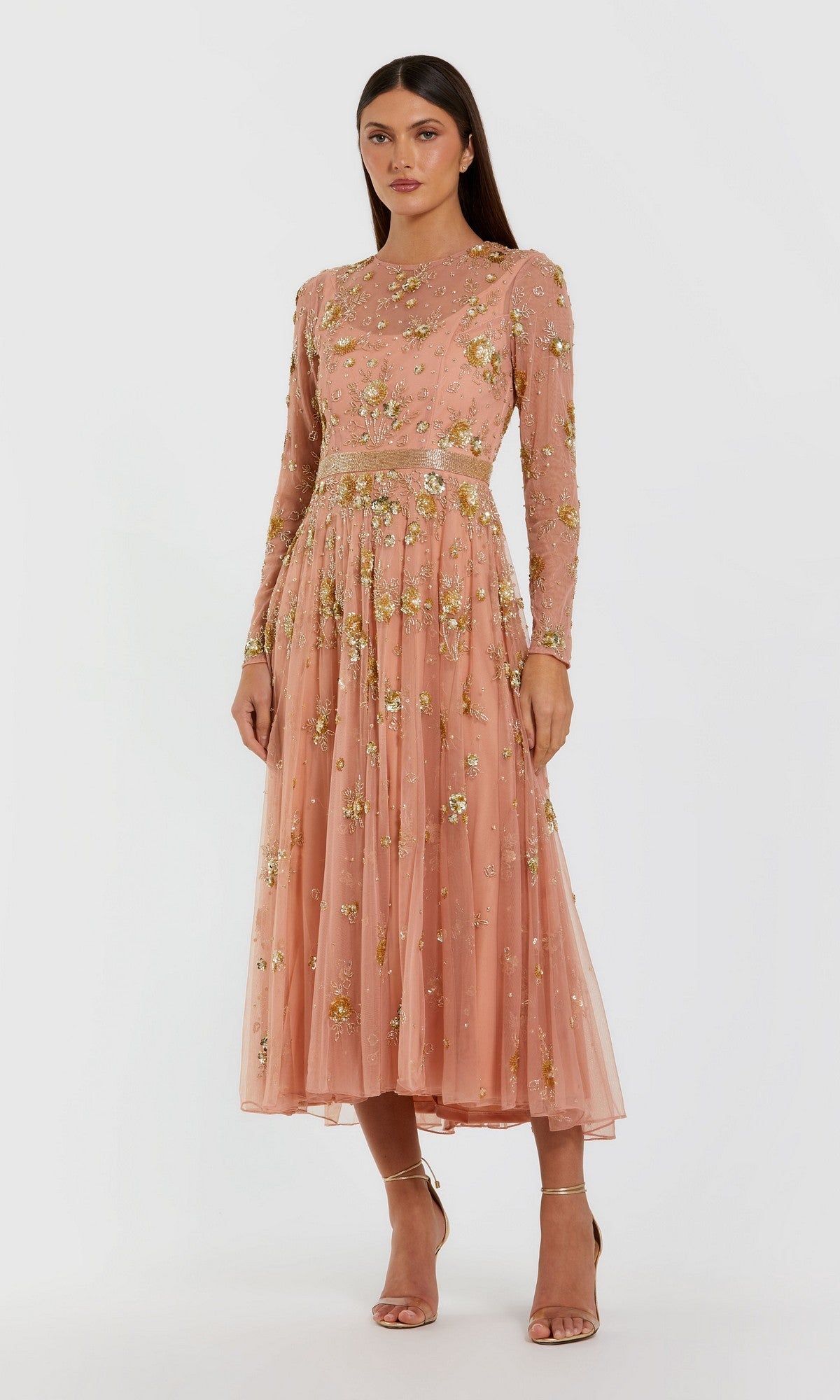 A woman wearing the Tea-Length Party Dress: Mac Duggal 6208 in peach, featuring long sleeves and floral embellishments with gold accents, stands against a plain light background—an elegant choice for a wedding guest dress.
