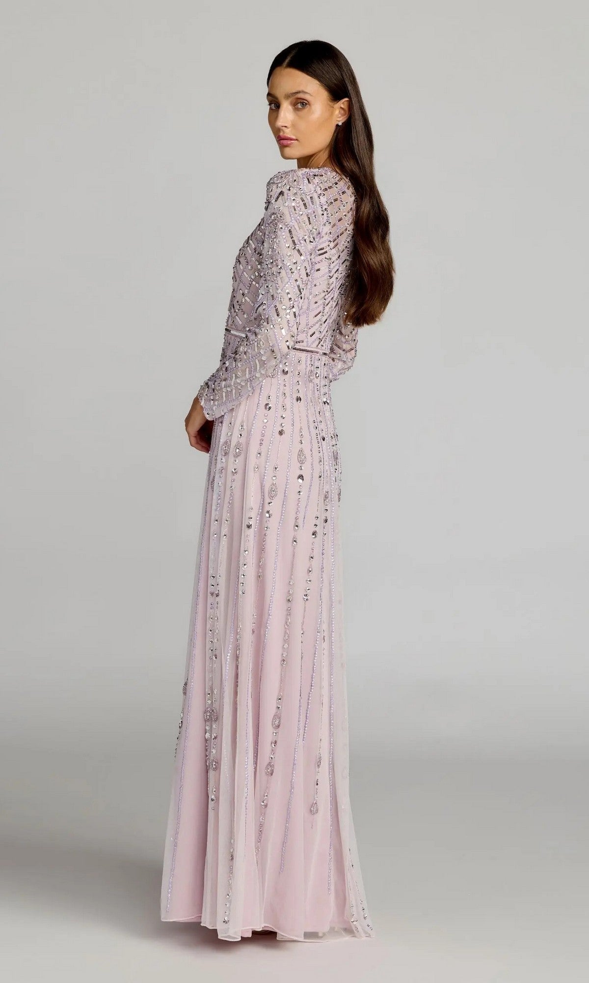 A woman stands sideways against a plain background, wearing the Mac Duggal 6236 Long Formal Dress—a floor-length gown with long sleeves, embellished with pale pink sequins and bead details.