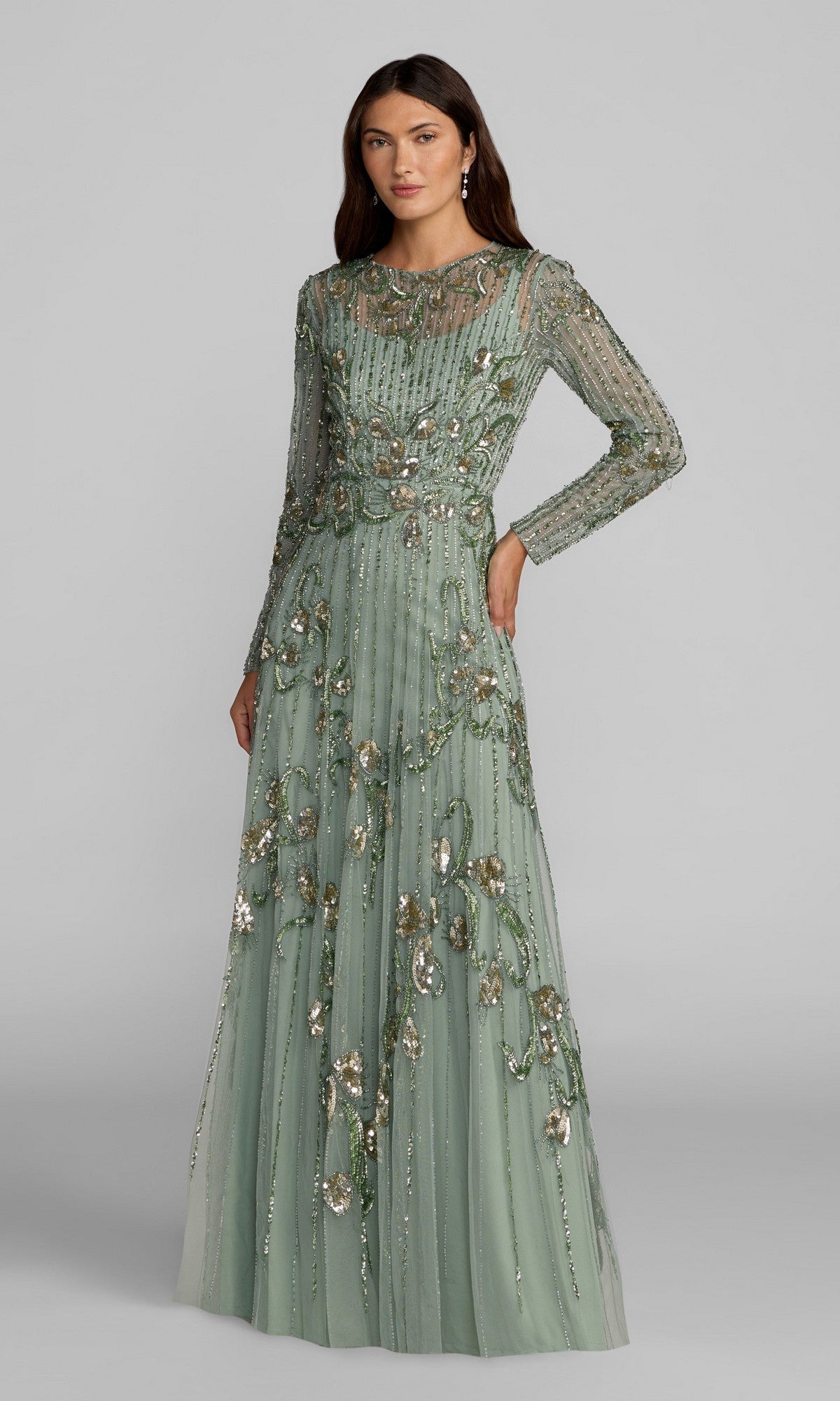 A woman stands against a plain gray background, wearing the Mac Duggal 6238 long formal dress in sage, featuring sheer sleeves and intricate beaded floral embellishments with delicate sequin embroidery.