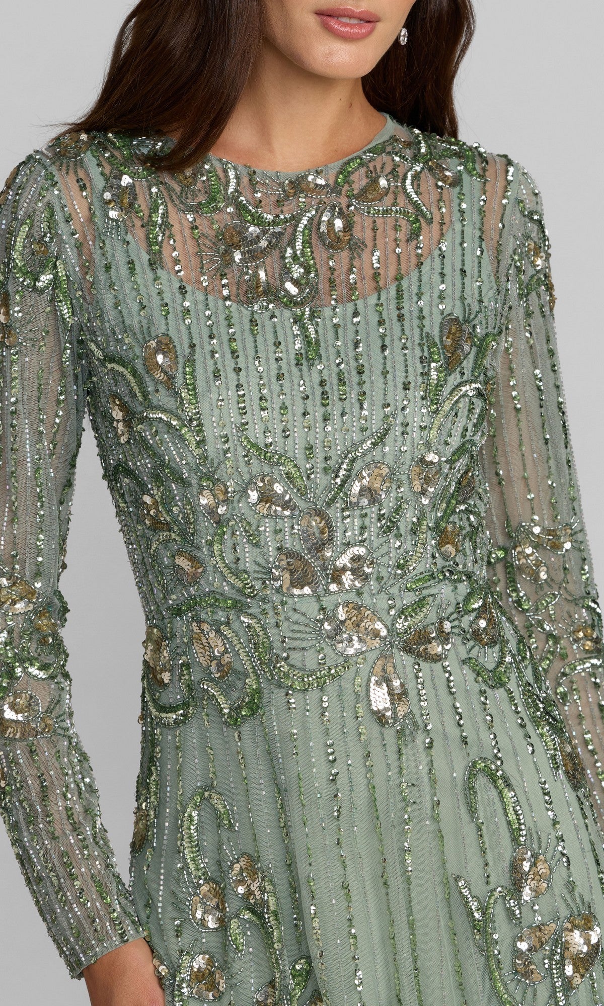 A woman wearing the Mac Duggal 6238 long formal dress, featuring long sleeves and sage green fabric adorned with silver and green sequin embroidery, photographed from the shoulders to the hips.