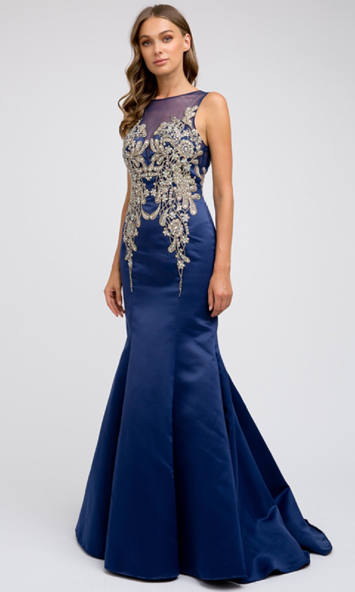 A woman wearing the Juliet 623—a sleeveless, floor-length navy blue prom dress with gold embroidery on the bodice—stands against a plain light background.