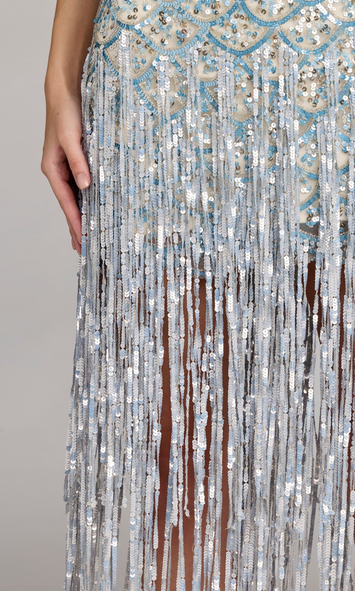 A person wearing the Long Formal Dress: Mac Duggal 6251, featuring silver beading, sequins, and fringe, shown from hip to knee with one hand at their side.