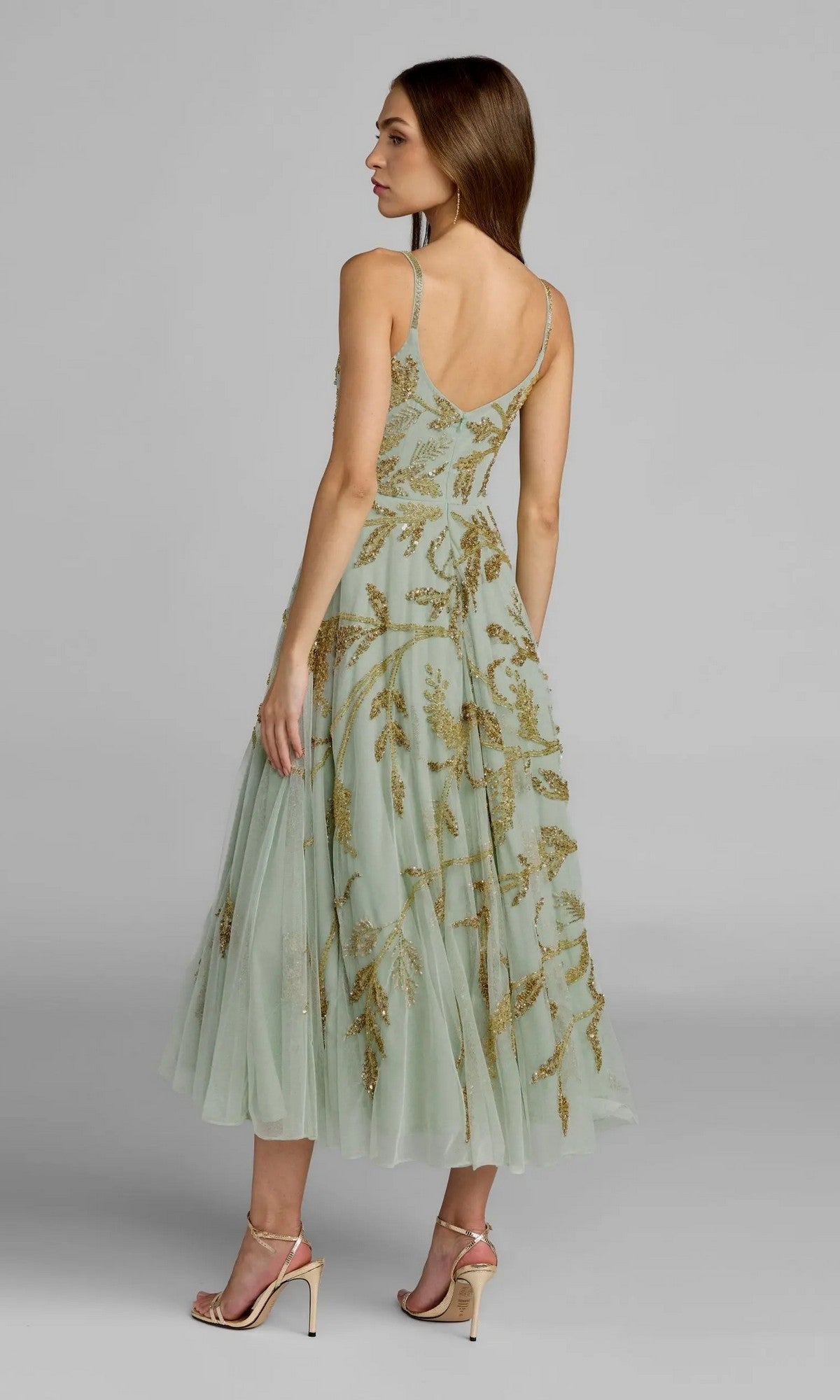 A woman is seen in profile, her back slightly turned, wearing the Mac Duggal 6255 Tea-Length Party Dress—a light green, sleeveless gown featuring gold beaded floral embroidery.
