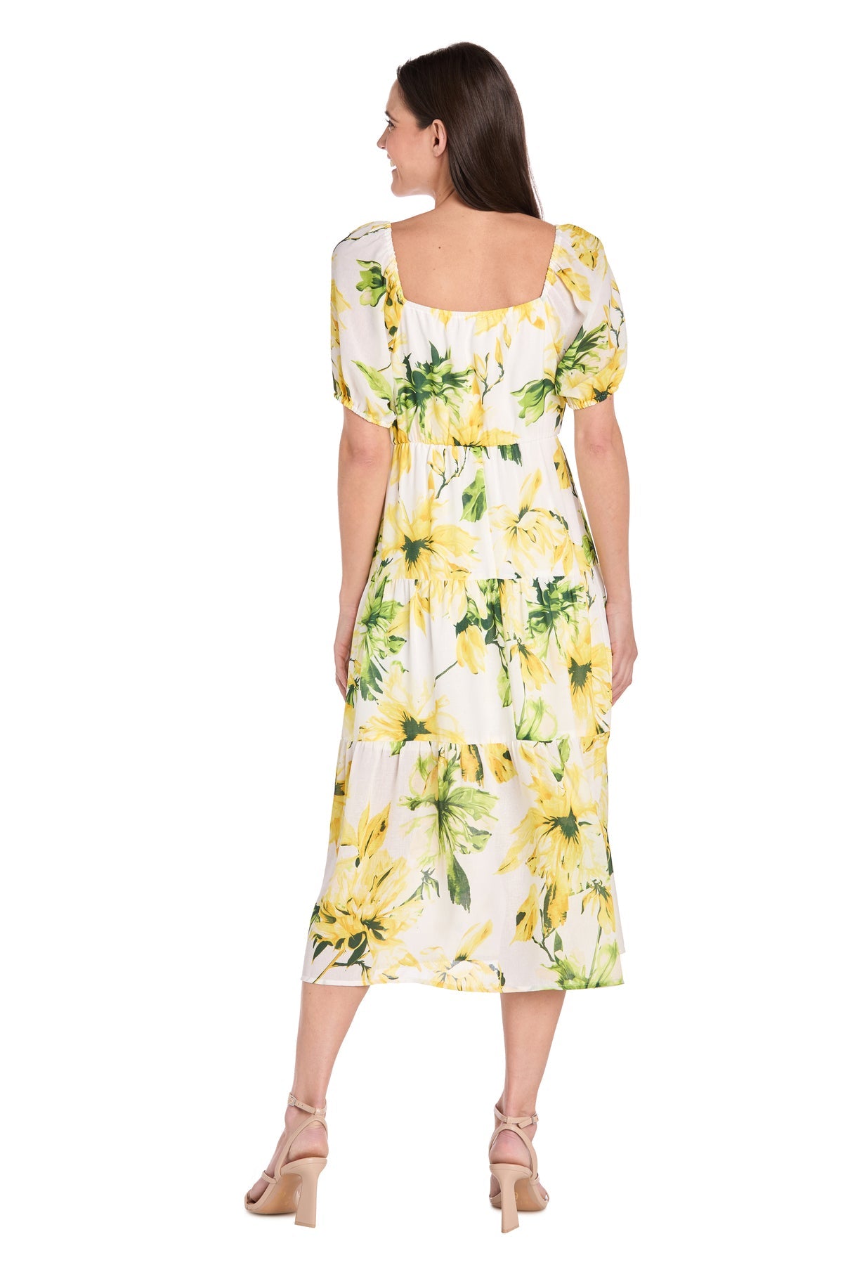 A woman stands facing away, wearing the R&M 6672P Petite Midi Yellow Print Party Dress with short puff sleeves and beige heeled sandals against a white background.