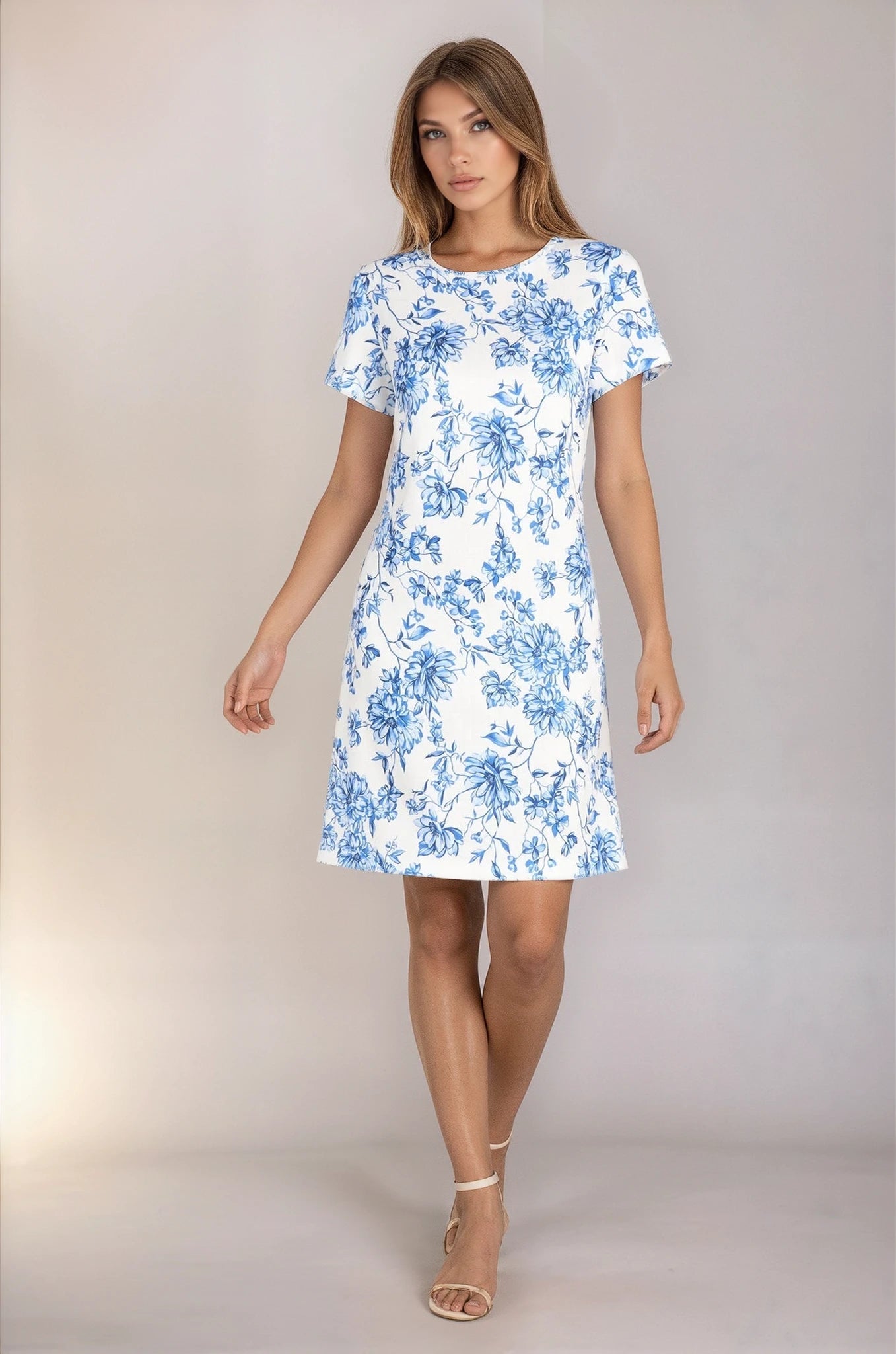 A woman wears the R&M Richards 6674 short sleeve party dress in blue and white floral and beige ankle-strap heels, standing against a plain background.
