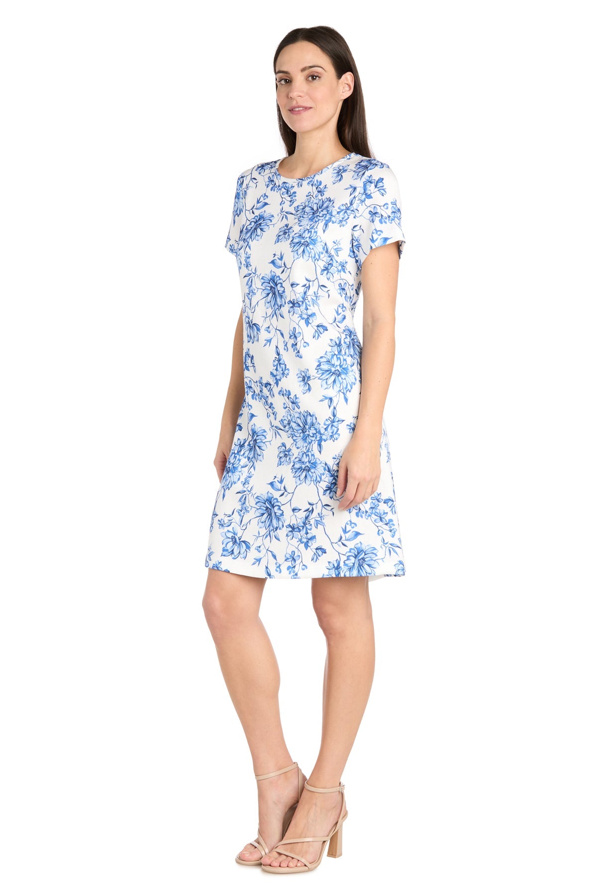 A woman models the R&M Richards 6674P Petite Print Party Dress with short sleeves and neutral heels, standing against a plain white background.