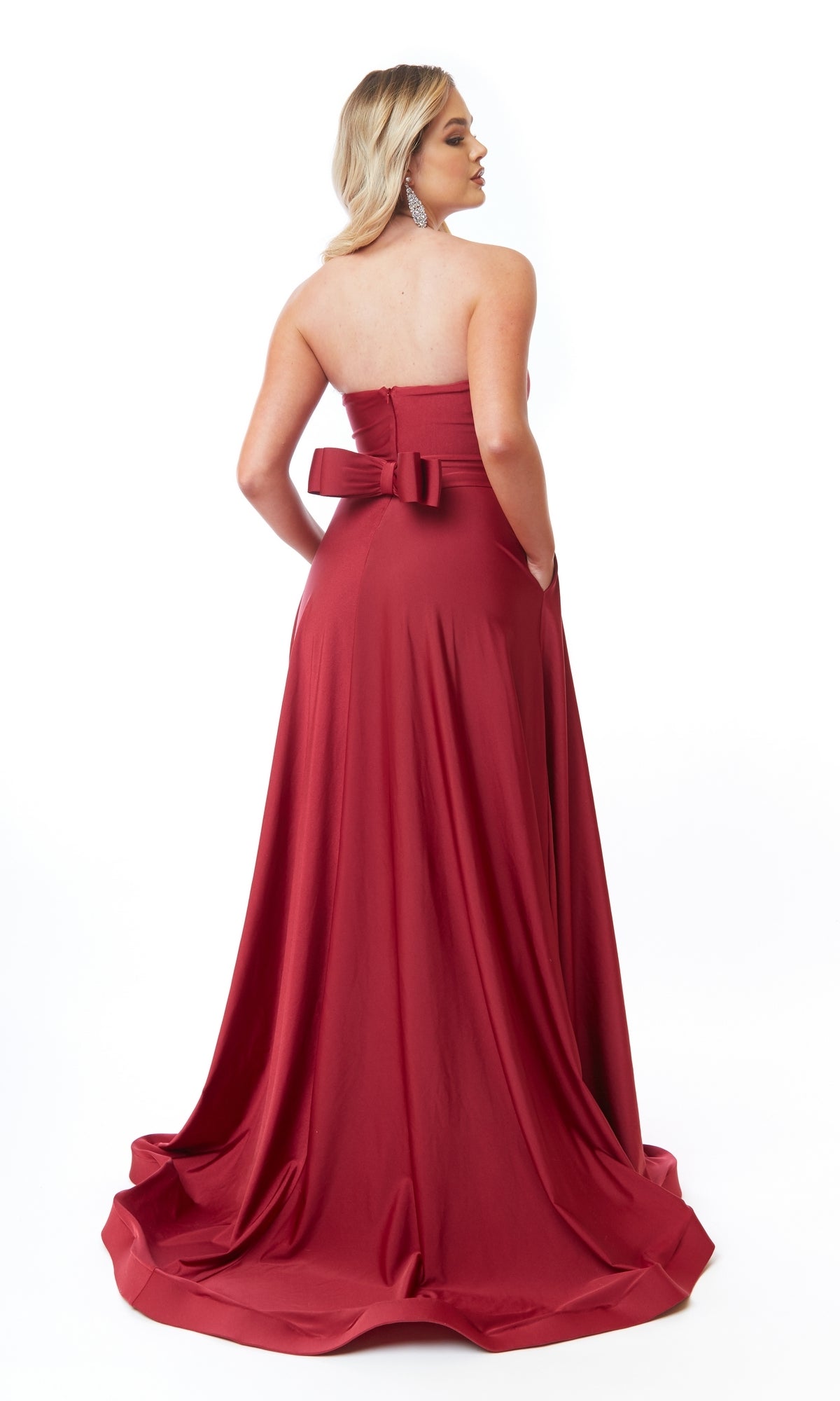 A person faces away, wearing the Strapless Sweetheart Long Prom Dress: Atria 6705H—an elegant red A-line gown with a back bow—set against a plain white background.