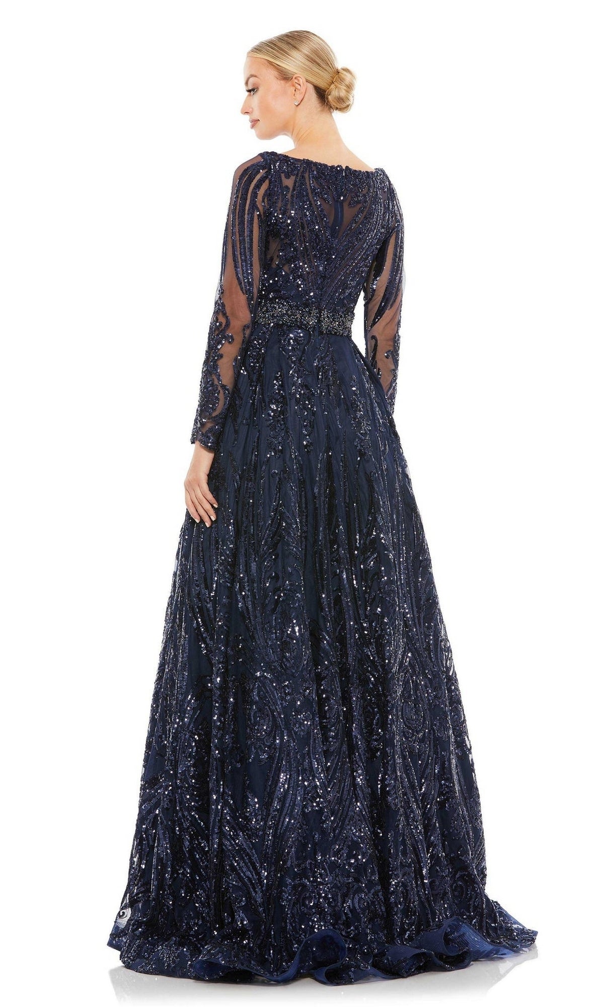 A woman in the Long Formal Dress 67113 by Mac Duggal, featuring midnight blue sequins and sheer long sleeves, stands facing away with her hair styled in a neat bun.