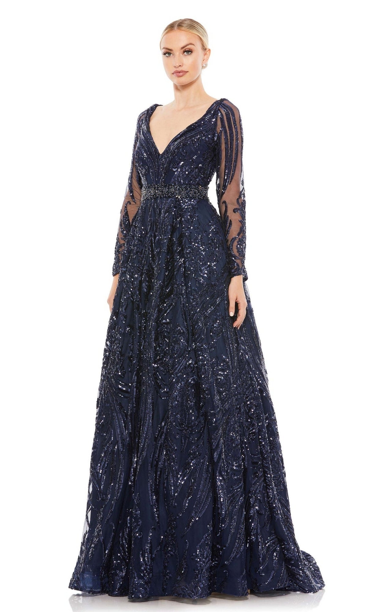 A woman wears the Long Formal Dress 67113 by Mac Duggal, featuring midnight blue fabric, intricate sequin detailing, and long sheer sleeves, as she stands against a white background.