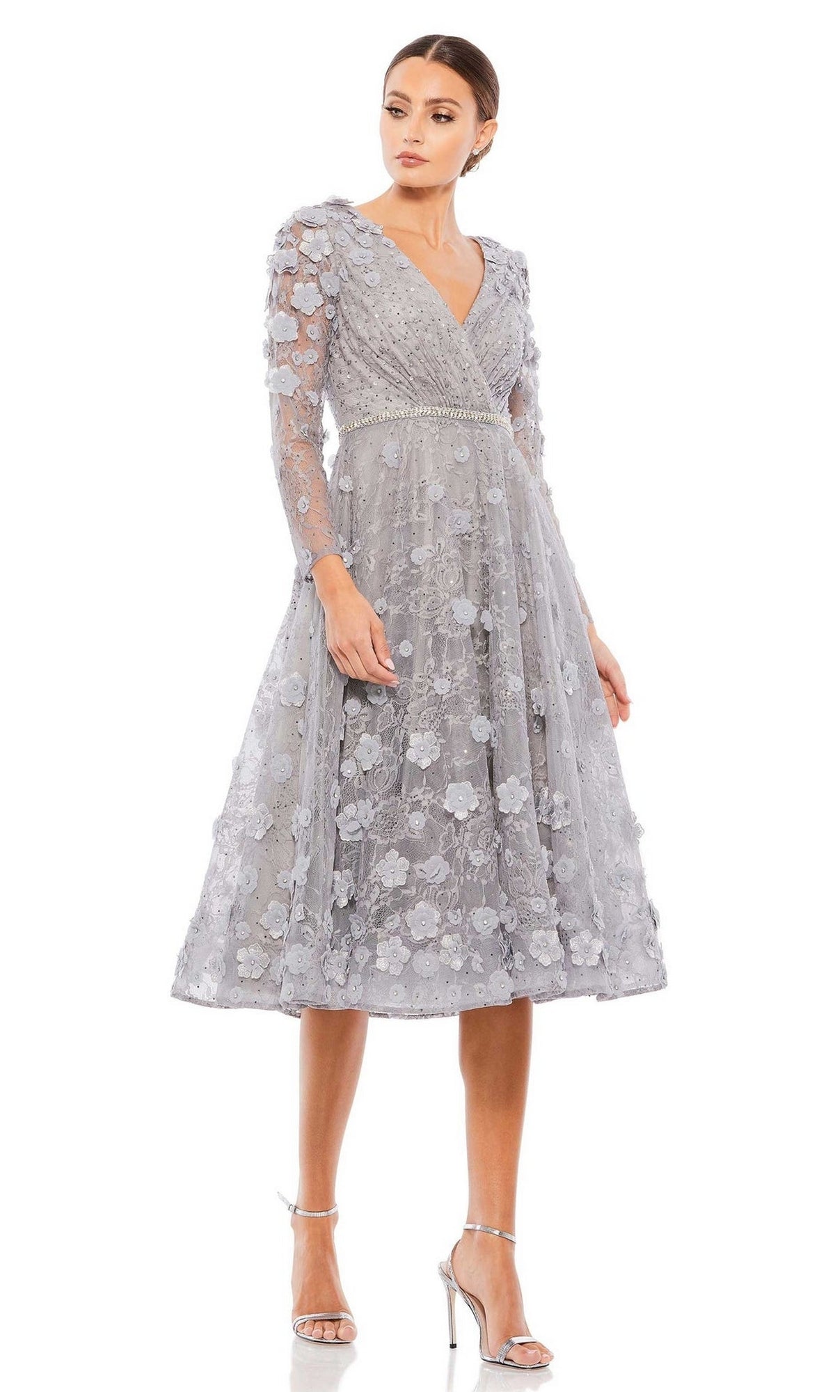 A woman in the Short Wedding Guest Dress 67387 by Mac Duggal, featuring floral appliqué details, long sleeves, and silver high heels, stands against a plain white background.