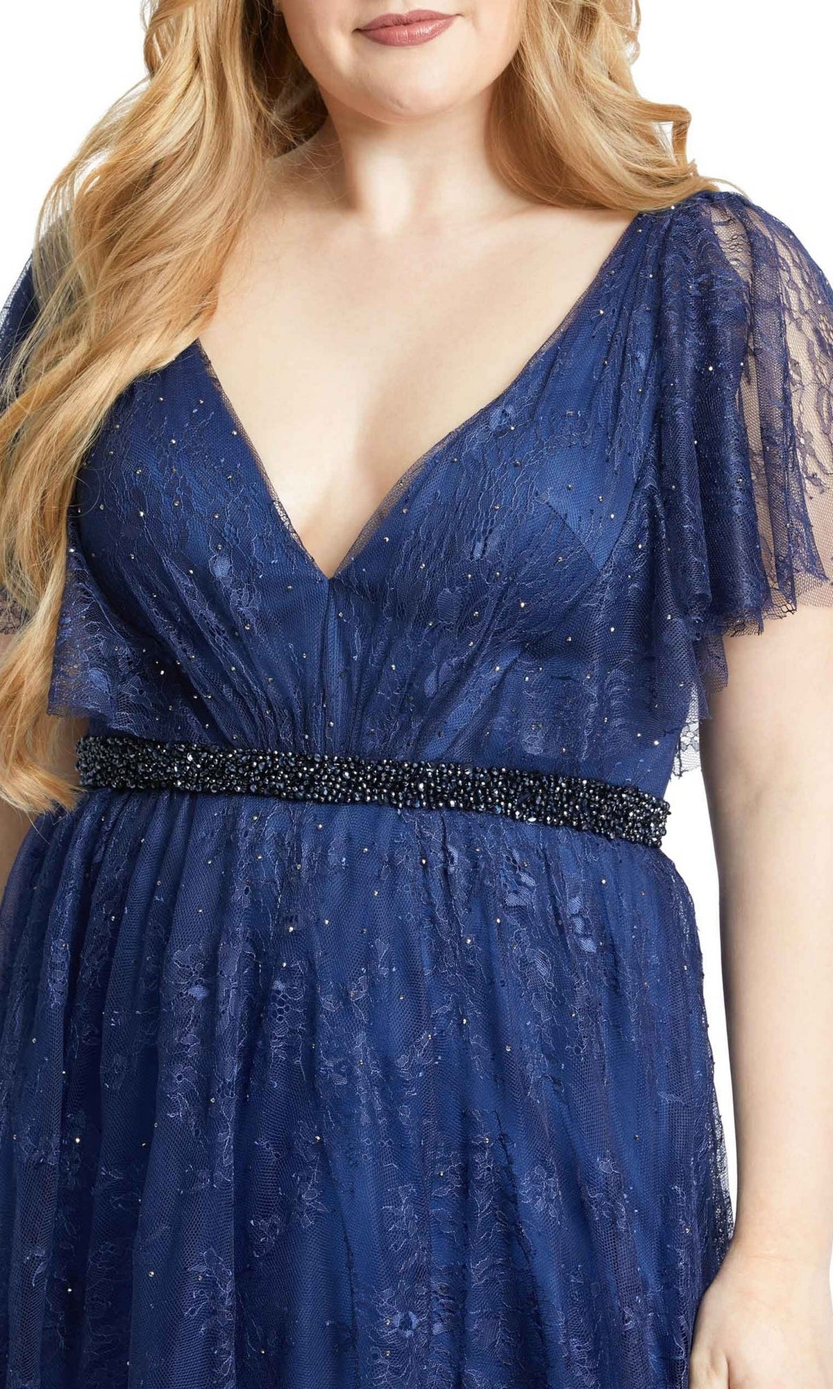 A woman wears the Long Plus-Size Prom Dress 67435 by Mac Duggal—a deep blue lace A-line gown with a V-neck, flutter sleeves, and a beaded black belt—elegantly shown from shoulders to hips.