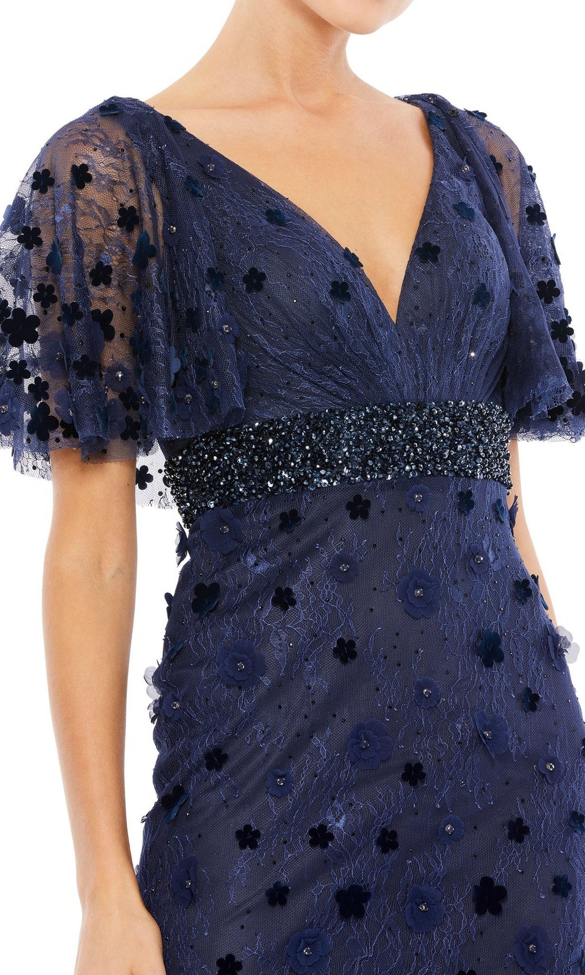 A woman wearing the Mac Duggal 67712 short-sleeve long formal dress in navy blue, featuring sheer sleeves, floral appliqué details, and a beaded waistband.