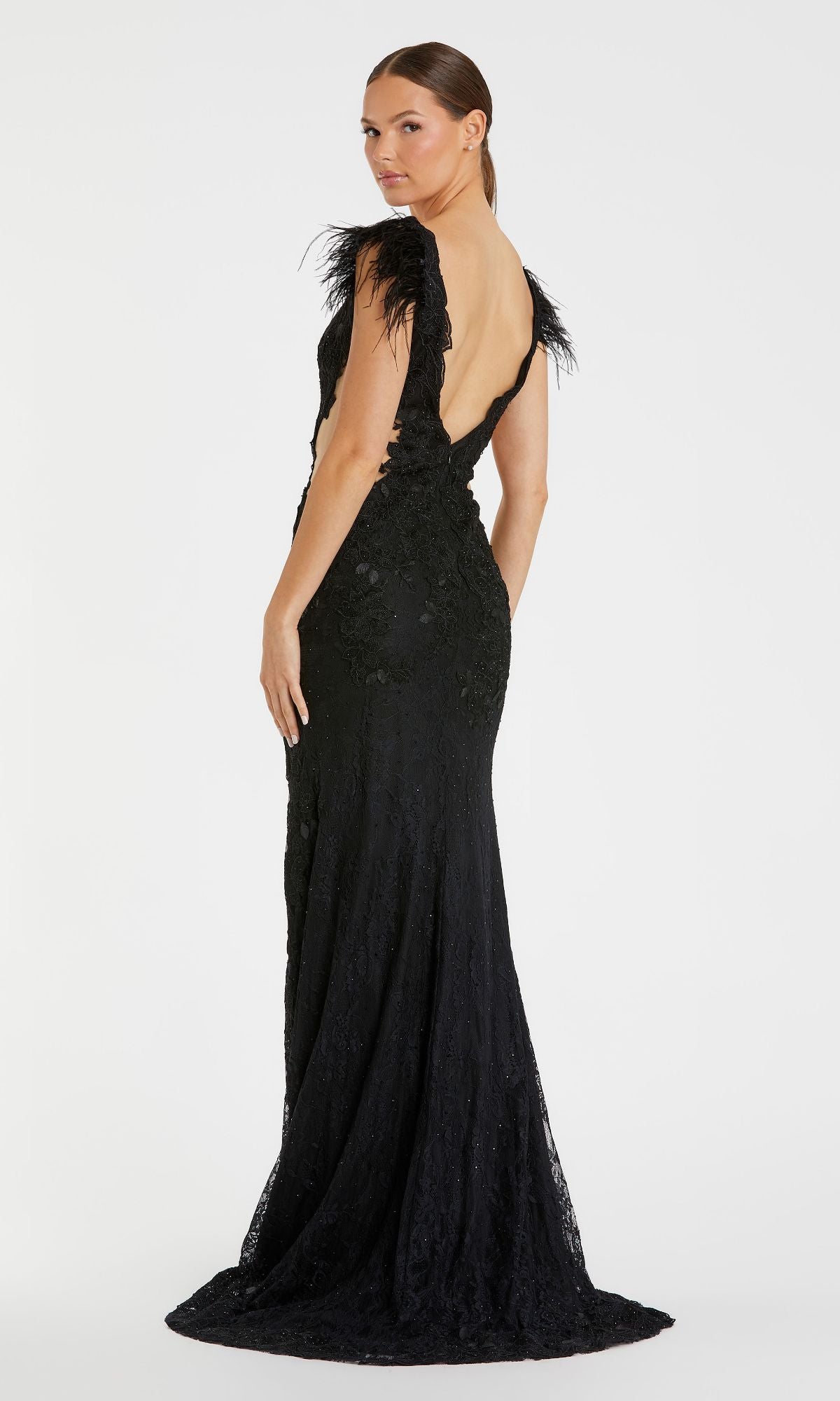 Woman wearing the Black Embroidered Formal Gown: Mac Duggal 67782, featuring feathered shoulder details, stands with her back partially to the camera against a plain white background.