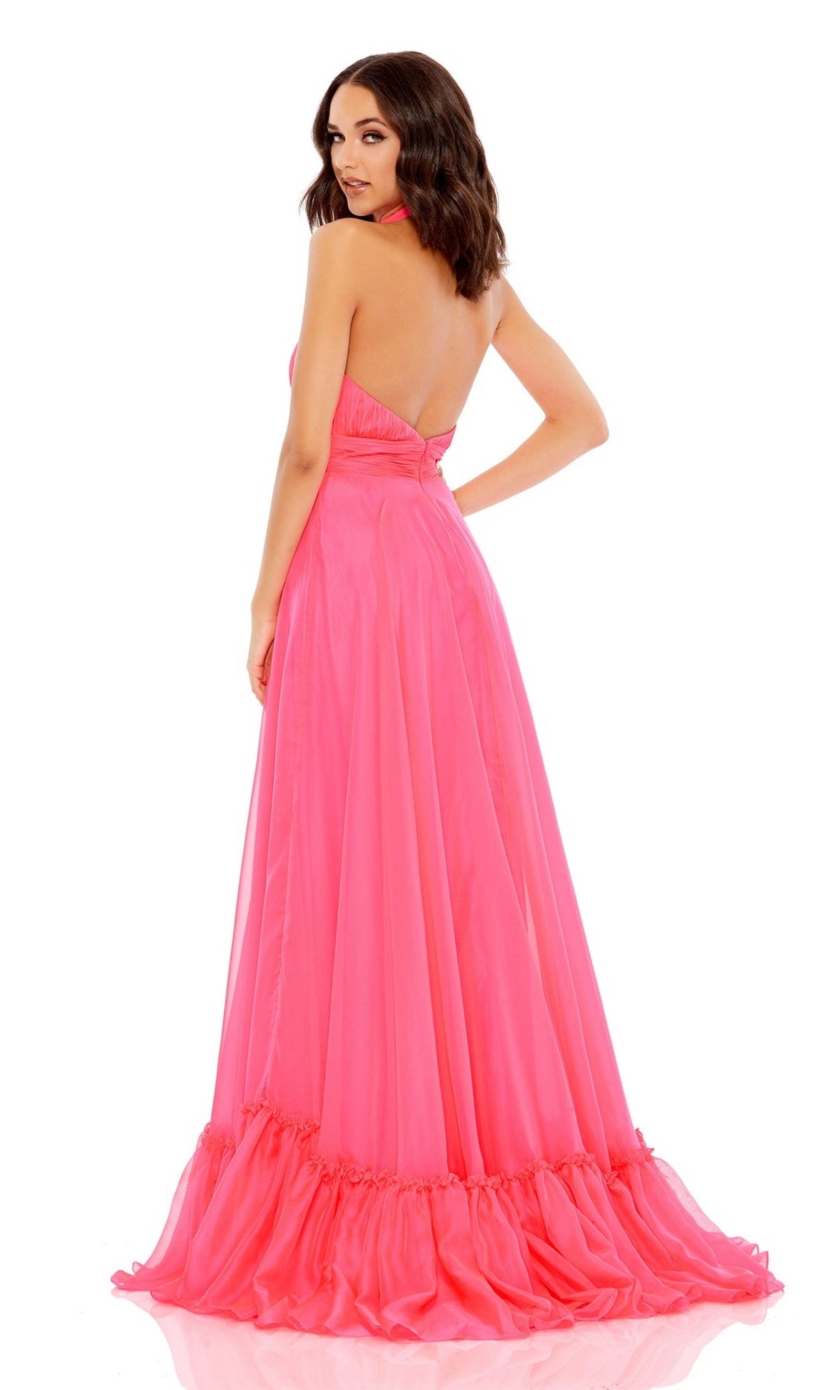 Woman in an open-back halter formal dress, Mac Duggal 67816, floor-length and bright pink with a ruffled hem, stands with her back to the camera against a white background.