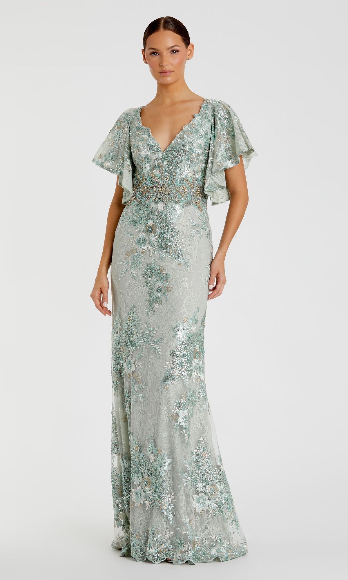 A woman wears the Mac Duggal 67842 Flutter-Sleeve Long Formal Dress—pale green, floor-length with floral embroidery, flutter sleeves, and a V-neckline—standing against a plain white background.