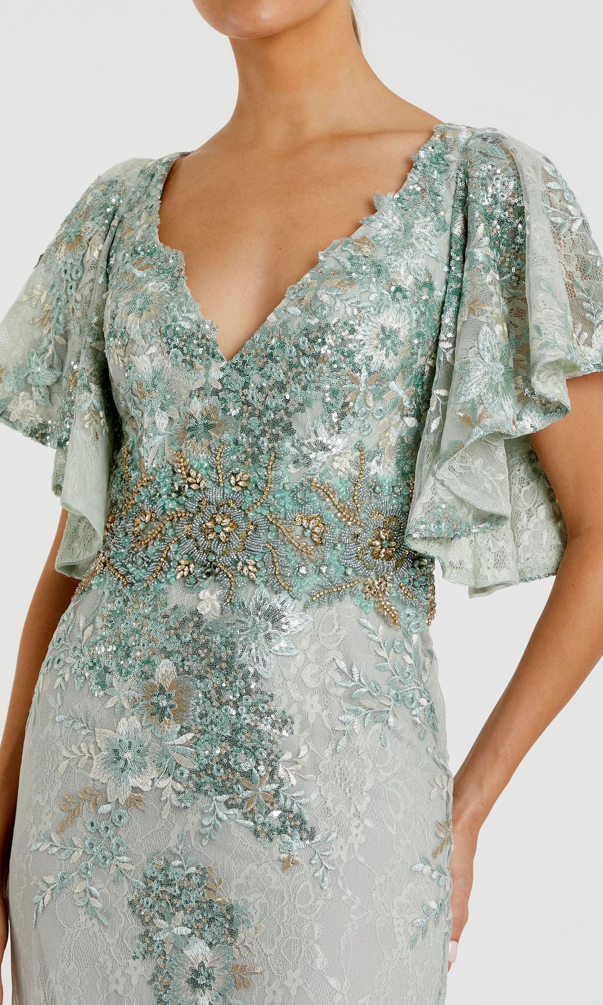 A woman wears the Mac Duggal 67842 Flutter-Sleeve Long Formal Dress in light blue-green, adorned with glitter lace, sequins and beads, flutter sleeves, and a deep V neckline.