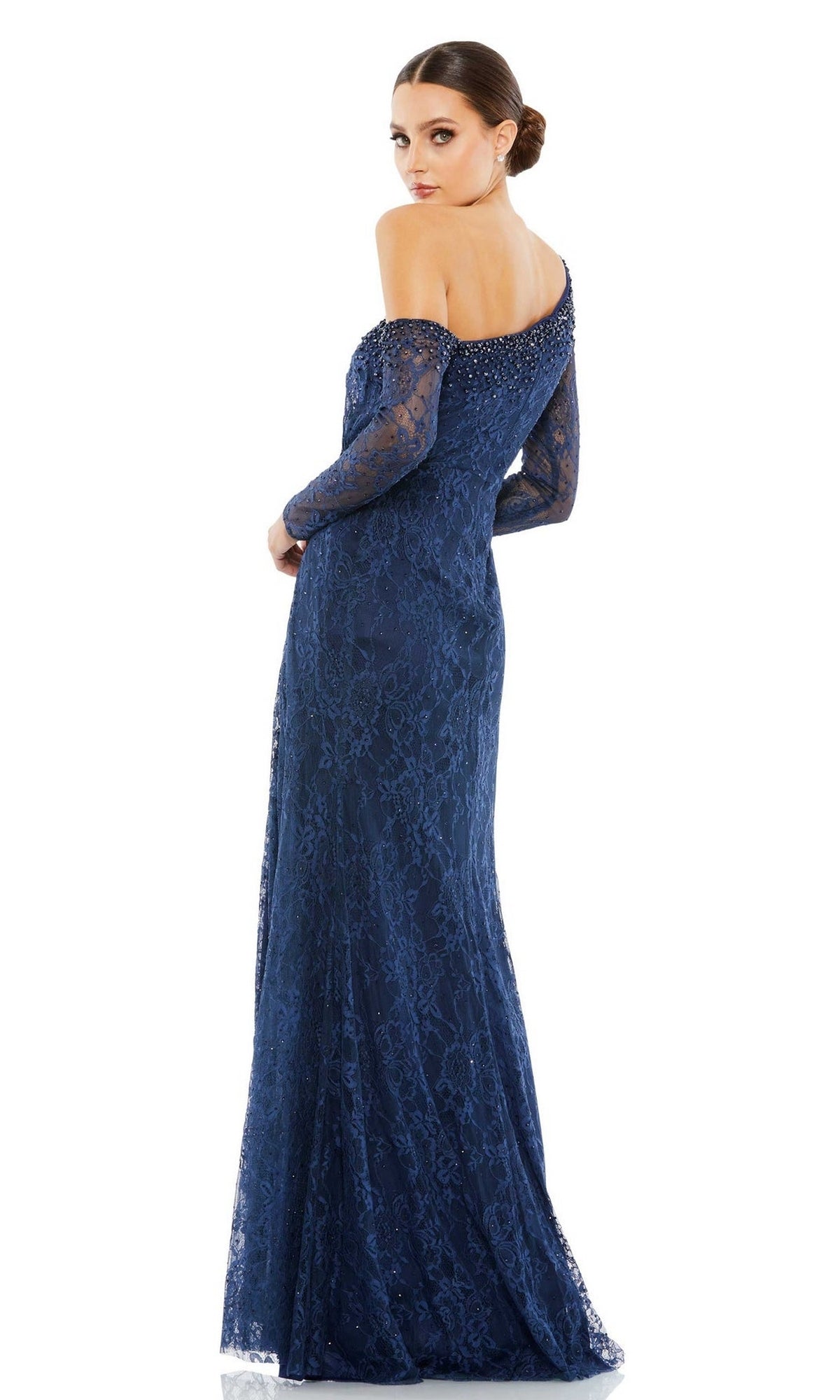 A woman wears the Long Formal Dress 67852 by Mac Duggal, a floor-length, off-the-shoulder navy lace gown with an embellished neckline and long sleeves, posing as she looks over her shoulder.