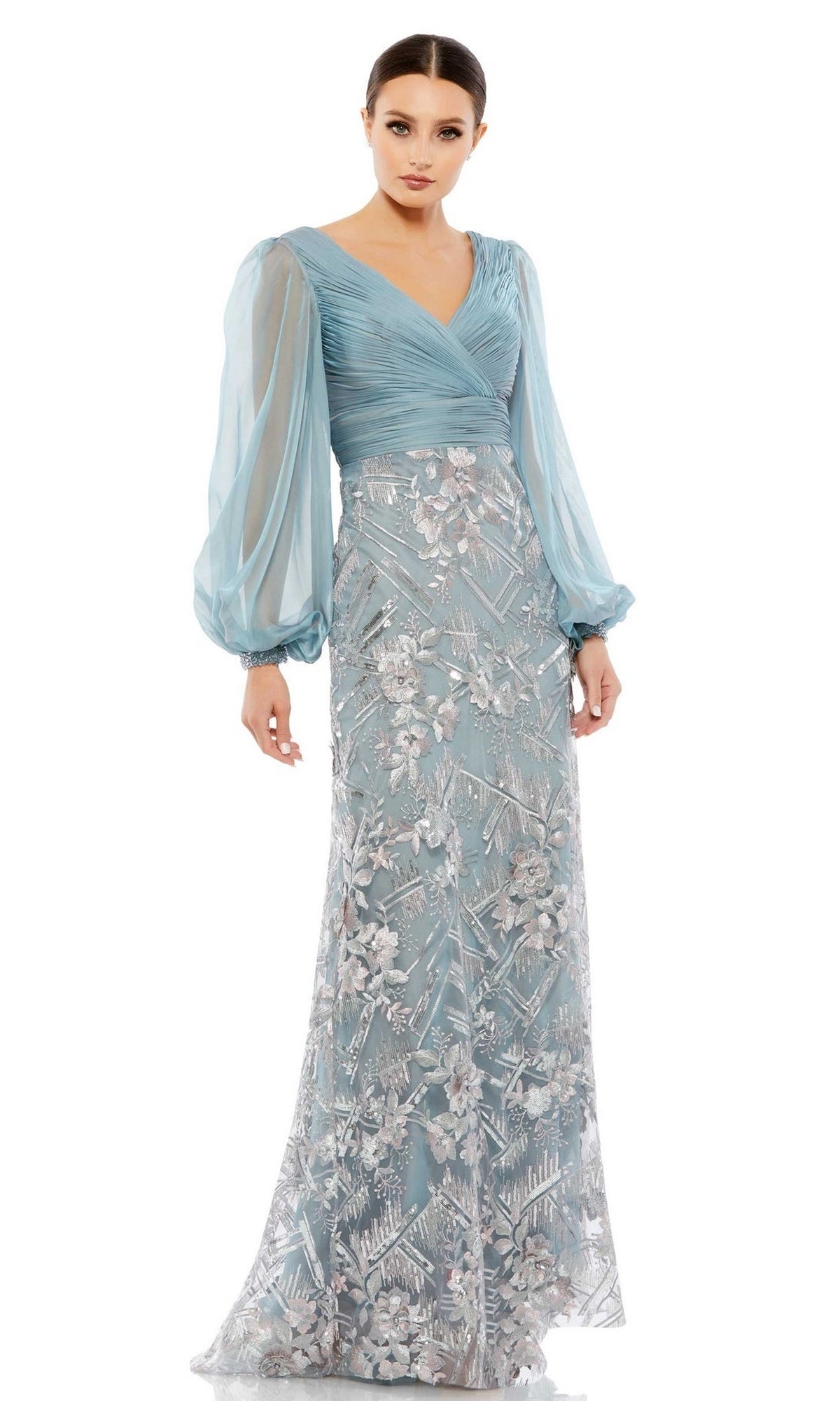 A woman wears the Long Formal Dress 67886 by Mac Duggal, a slate blue, floor-length gown featuring sheer puff sleeves and intricate silver floral embroidery on the skirt.