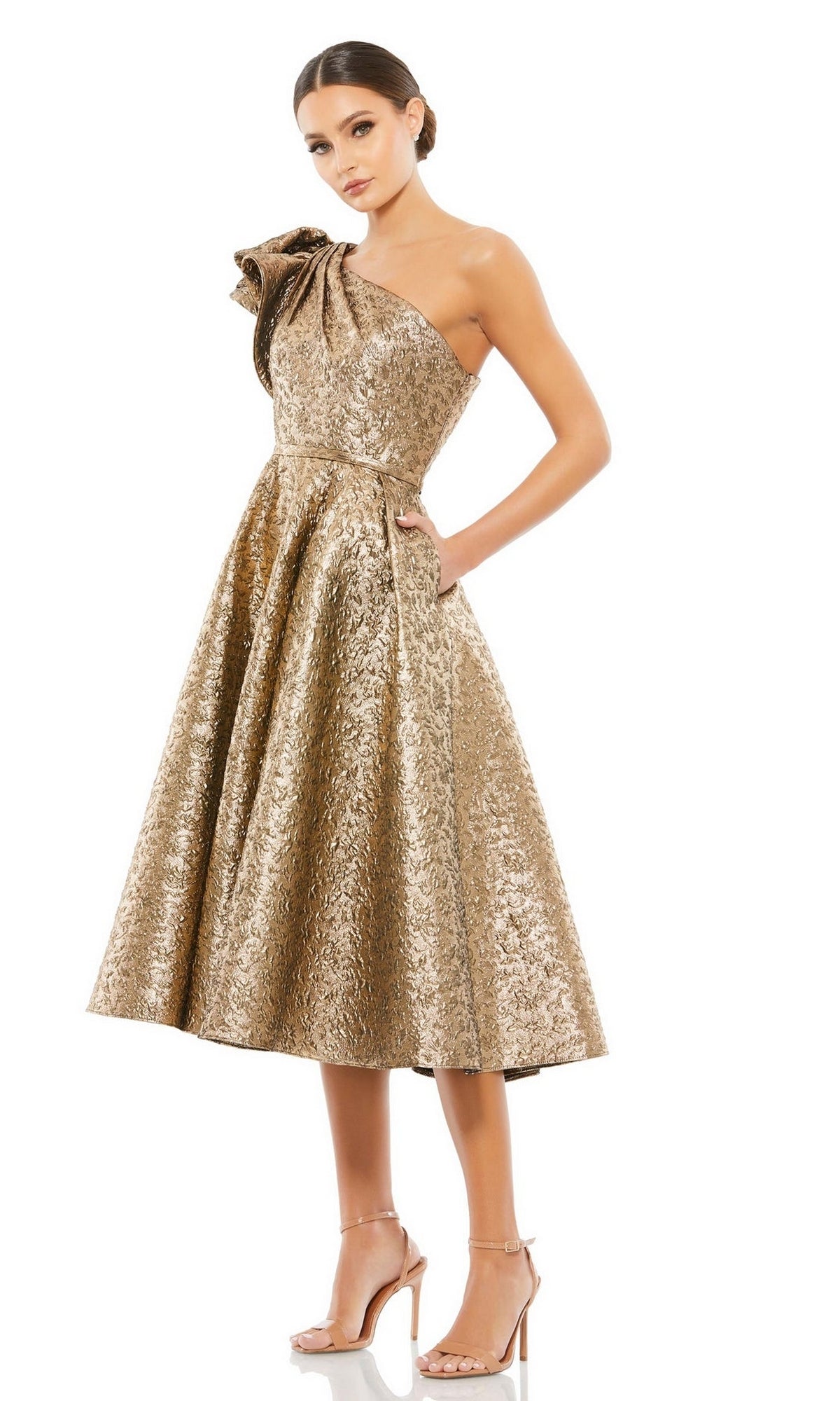 A woman wears the Mac Duggal 67906 metallic short wedding-guest dress, featuring a knee-length one-shoulder ruffled detail, styled with nude high-heeled sandals.