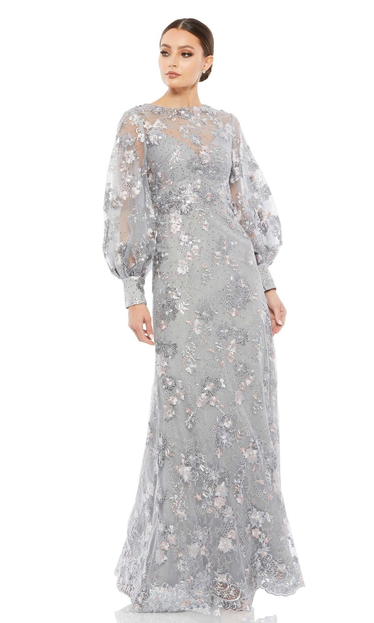 A woman wears the Long Formal Dress 67936 by Mac Duggal—a light blue floral lace gown with long sheer puff sleeves and a high neckline—standing against a white background.