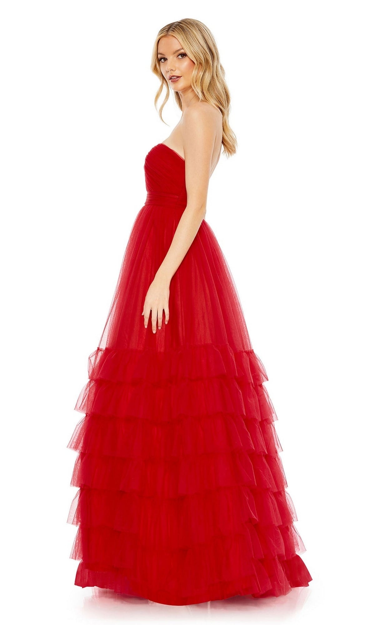 A woman stands sideways, glancing over her shoulder, wearing the Long Formal Dress 67999 by Mac Duggal—an elegant strapless, floor-length red tulle gown with a fitted bodice and tiered ruffle skirt.