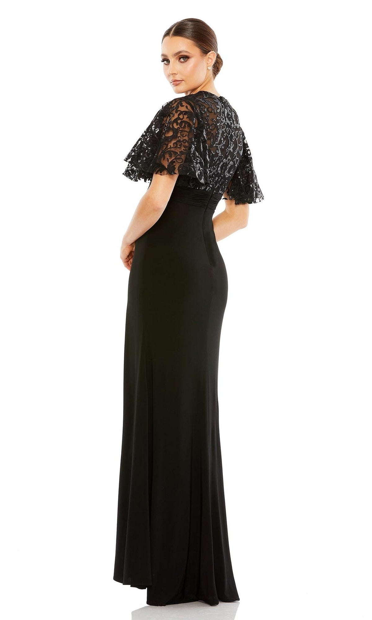 Woman wearing the Mac Duggal 68002 short sleeve black formal dress stands turned slightly to the side, looking back over her shoulder against a plain white background.