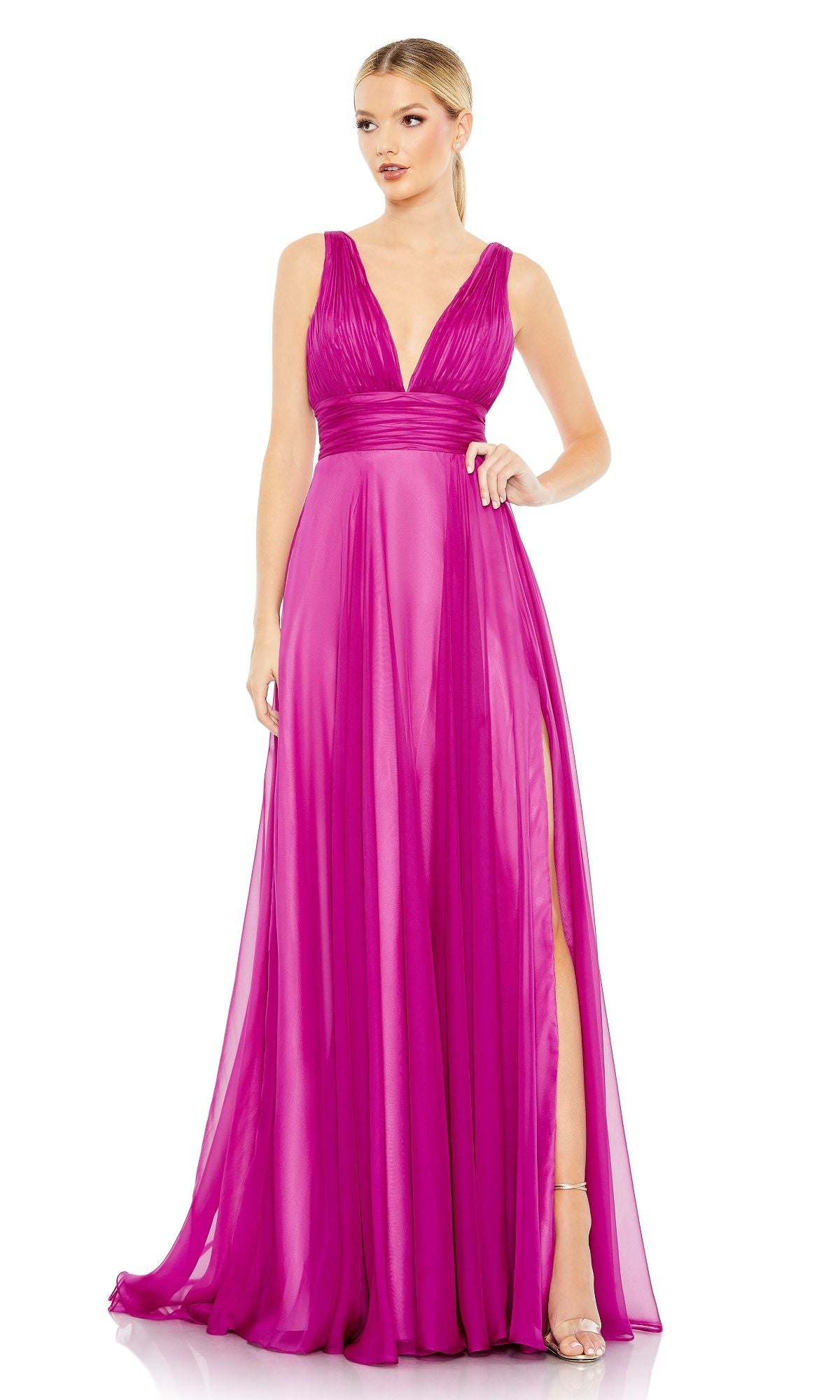 A woman poses on a white background wearing the Mac Duggal 68134—a floor-length fuchsia pink prom dress with an A-line skirt, sleeveless design, deep V-neckline, and a thigh-high slit.