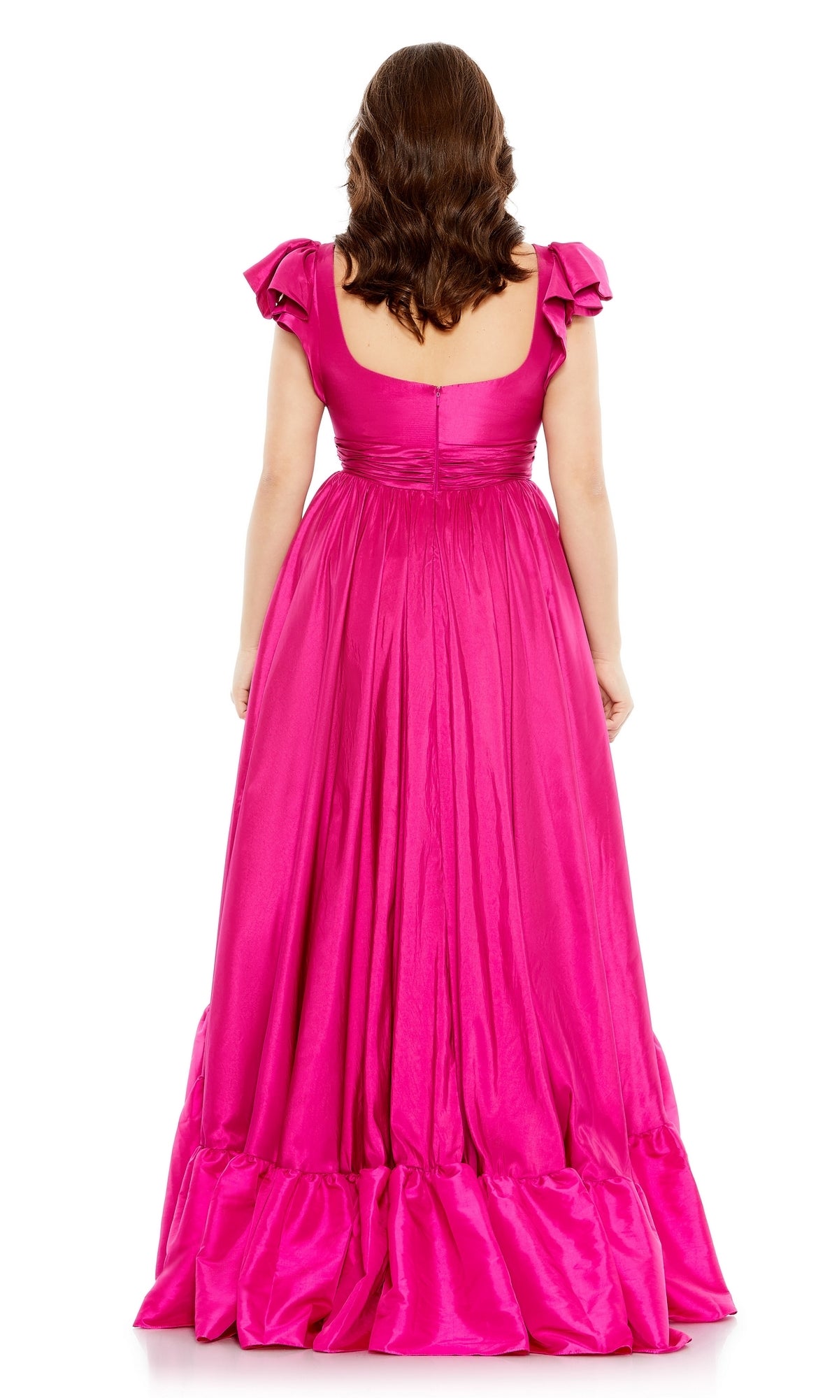 A woman with wavy brown hair models the Long Plus-Size Formal Dress 68150 by Mac Duggal in magenta pink, standing with her back to the camera against a white background.