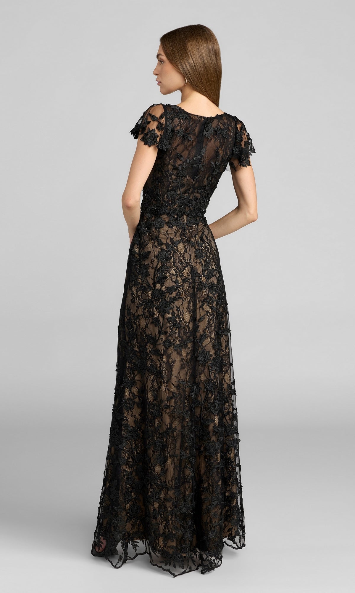A woman is seen from the back, standing against a plain gray background, wearing the Mac Duggal 68192 Long Beaded Formal Dress—a floor-length black evening gown with short sleeves.