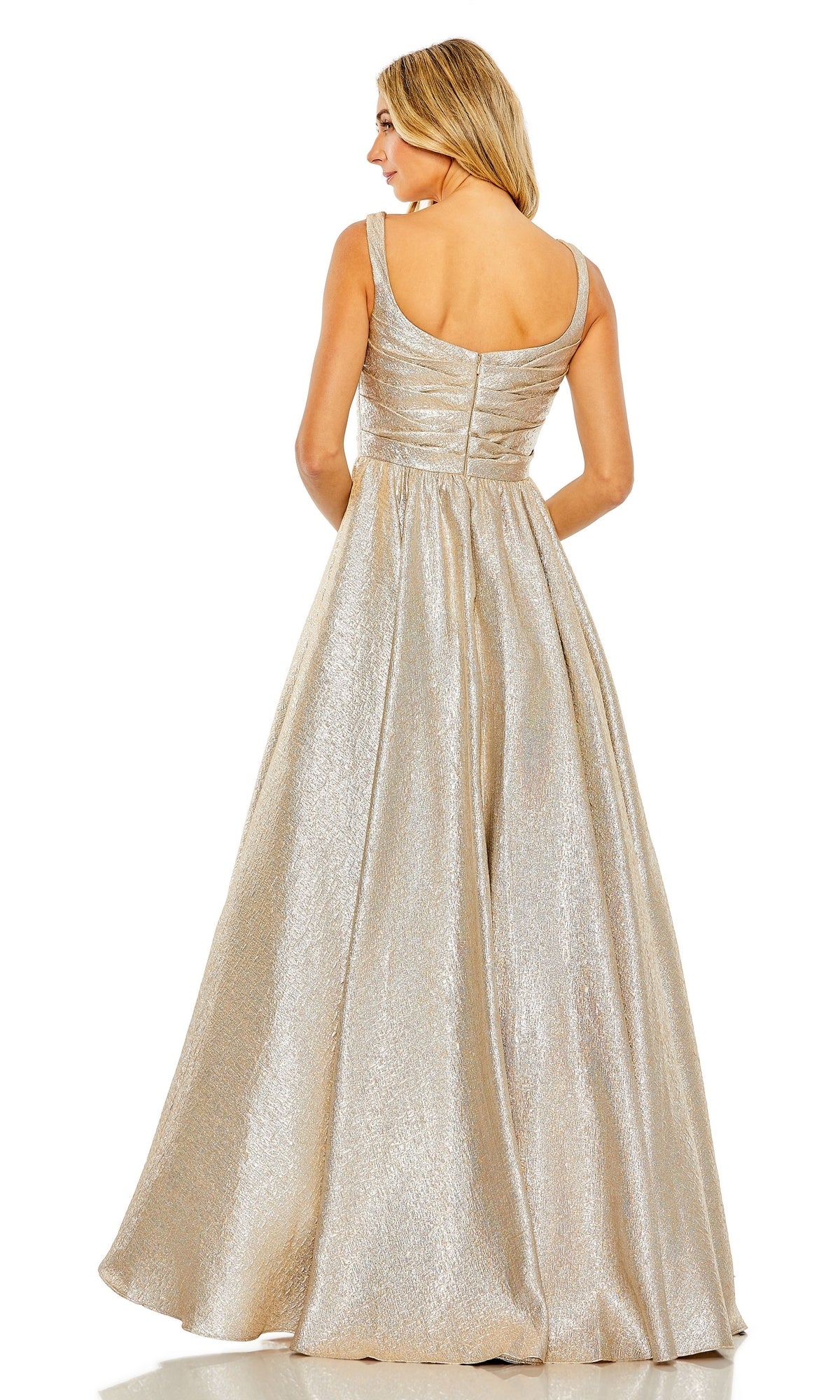 A woman stands facing away, wearing the Mac Duggal 68349 Long Glitter Prom Ball Gown—a sleeveless, floor-length A-line dress with a fitted bodice and flared skirt in striking metallic gold.
