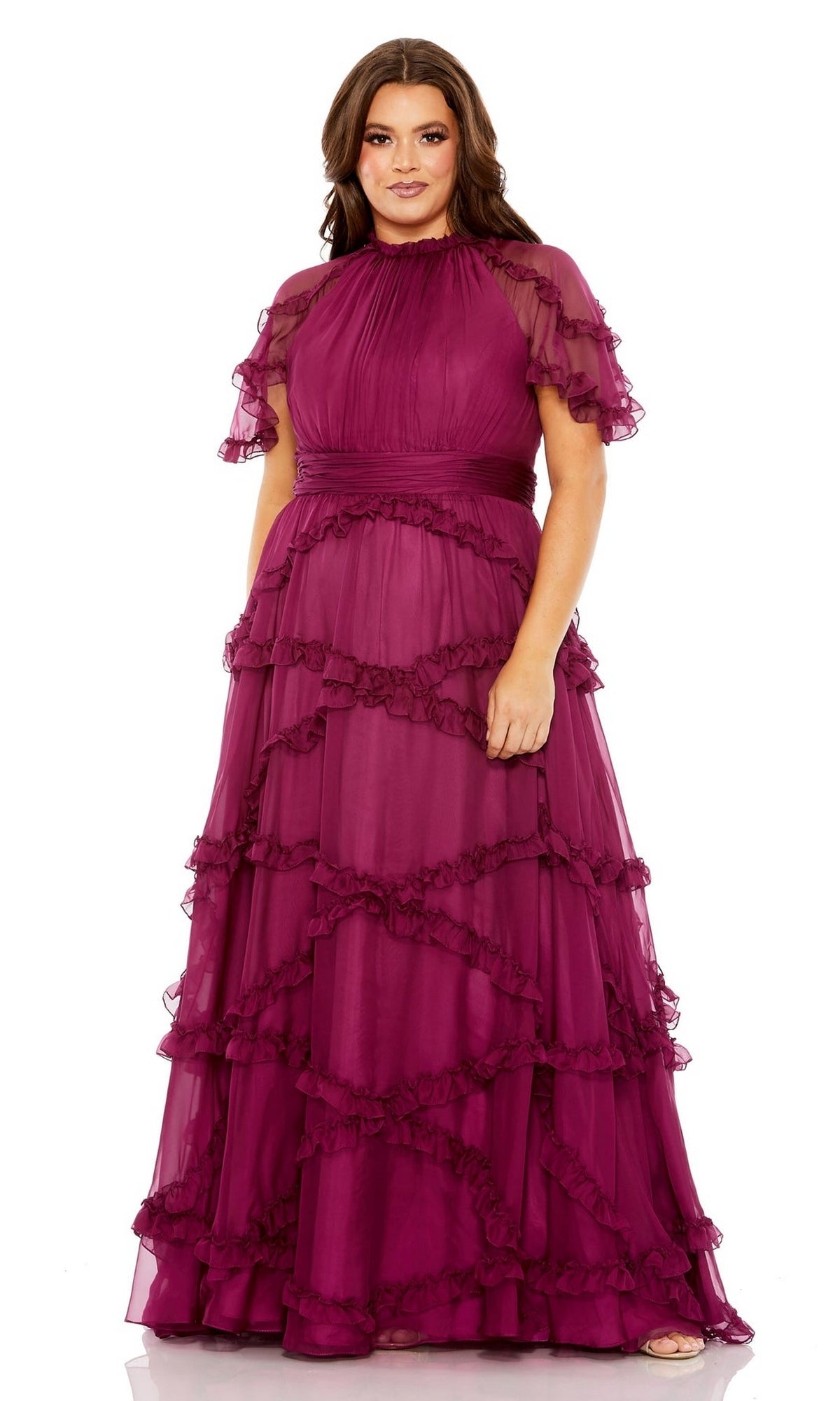 A woman models the Long Plus-Size Prom Dress 68424 by Mac Duggal—a floor-length, dark magenta gown with short sheer sleeves and layered ruffle tiers—posing against a plain white background.