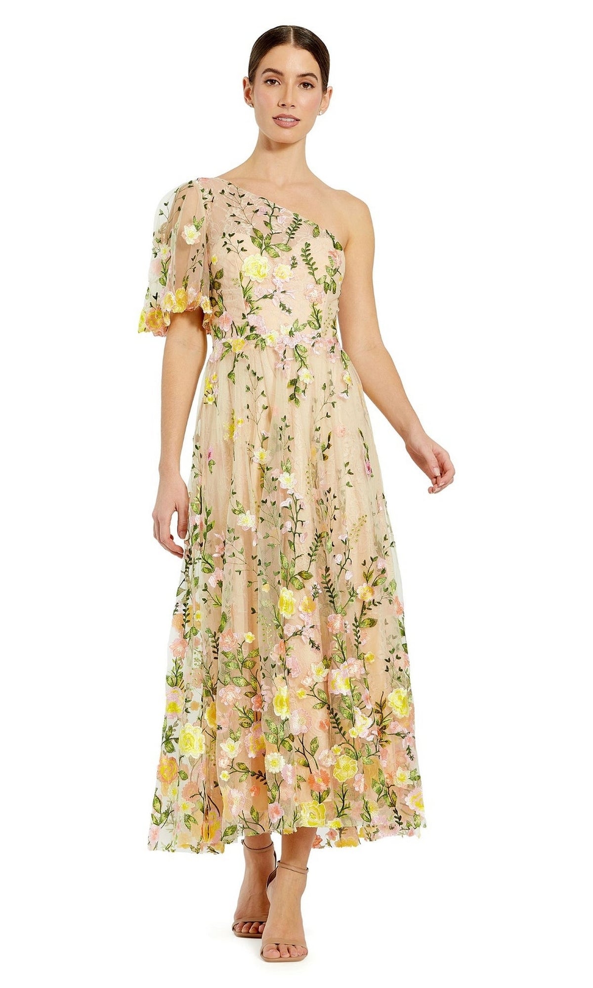A woman stands against a plain white background wearing the Mac Duggal 68607 one-shoulder midi party dress with pastel floral embroidery and beige heeled sandals.