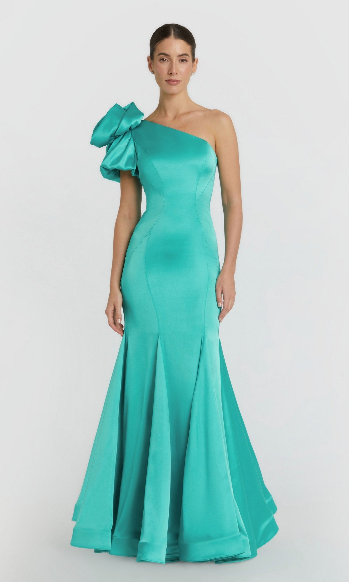A woman stands against a white background wearing the Mac Duggal 68703 long formal dress in teal, featuring a fitted, floor-length satin design with an asymmetrical neckline and a statement ruffle on one shoulder.